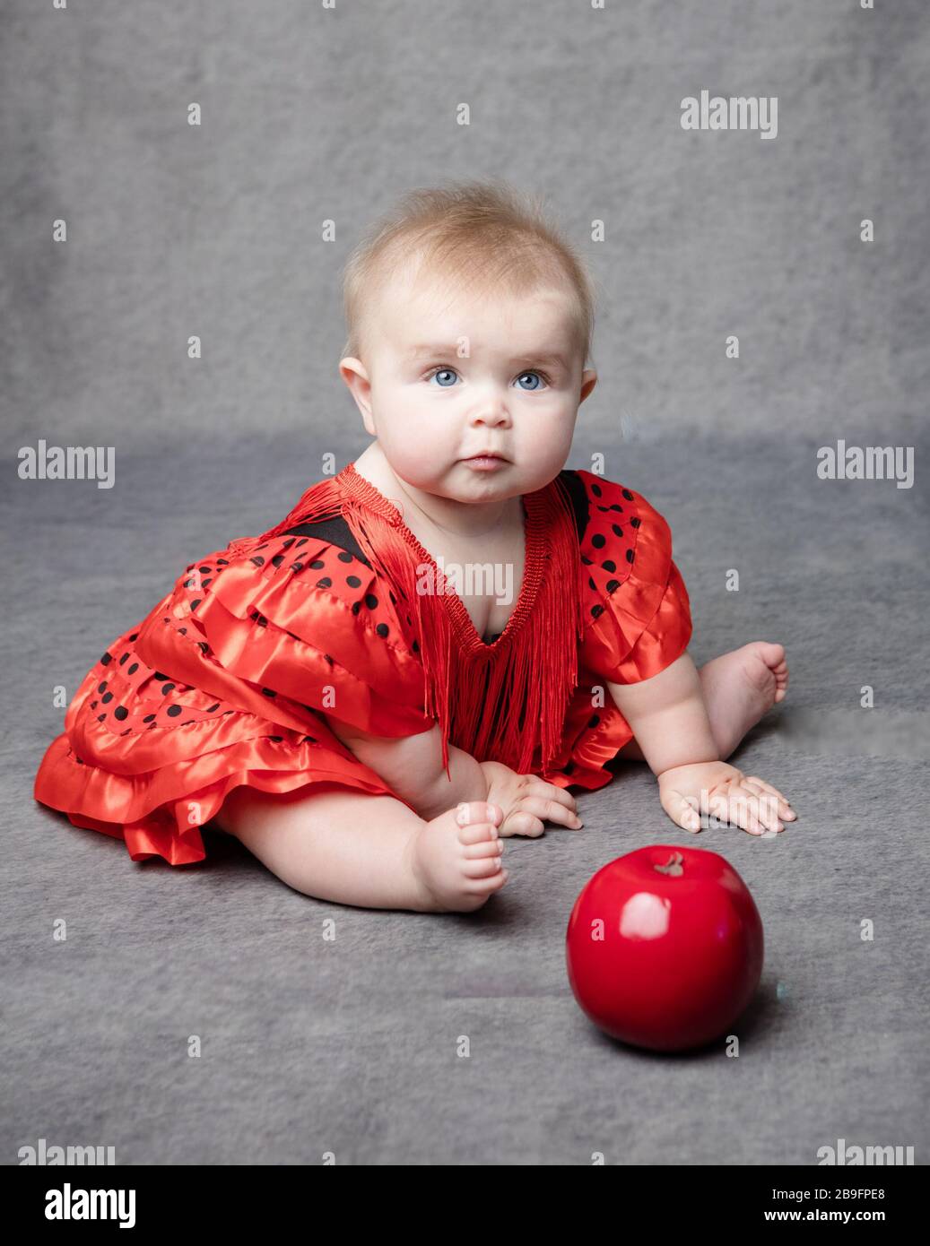 Assis bébé fille dans la robe rouge avec pomme sur fond gris de studio Banque D'Images