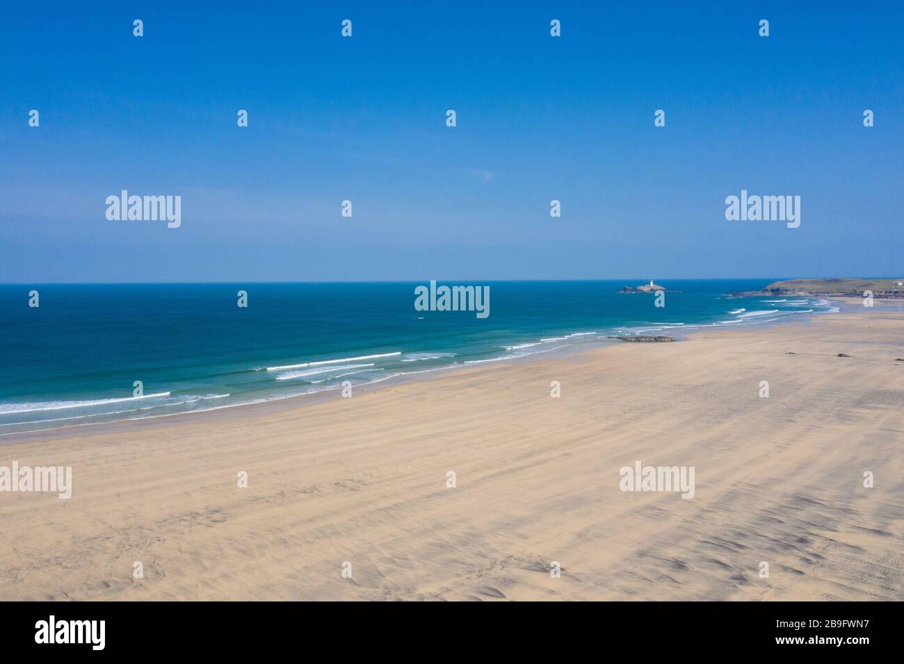 Photo aérienne d'une plage de Gwithian vide avec vagues briser et phare de rêve en arrière-plan sur une journée de ciel bleu Banque D'Images
