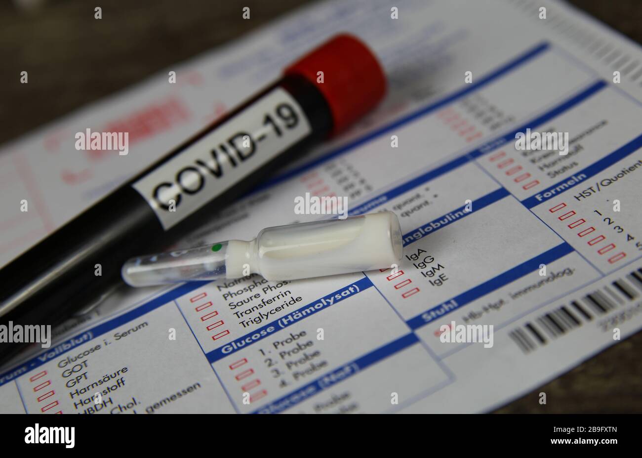 Viersen, Allemagne - 22 mars. 2020: Gros plan du tube d'échantillon de sang isolé avec le mot covid-19 et l'ampoule de verre de médicament blanc. Demande de test de laboratoire floue Banque D'Images