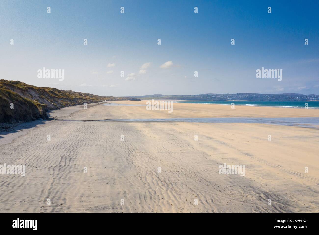 Photo aérienne d'une plage de Gwithian vide avec vagues déferlantes et dunes de sable sur un ciel bleu avec St ives en arrière-plan Banque D'Images