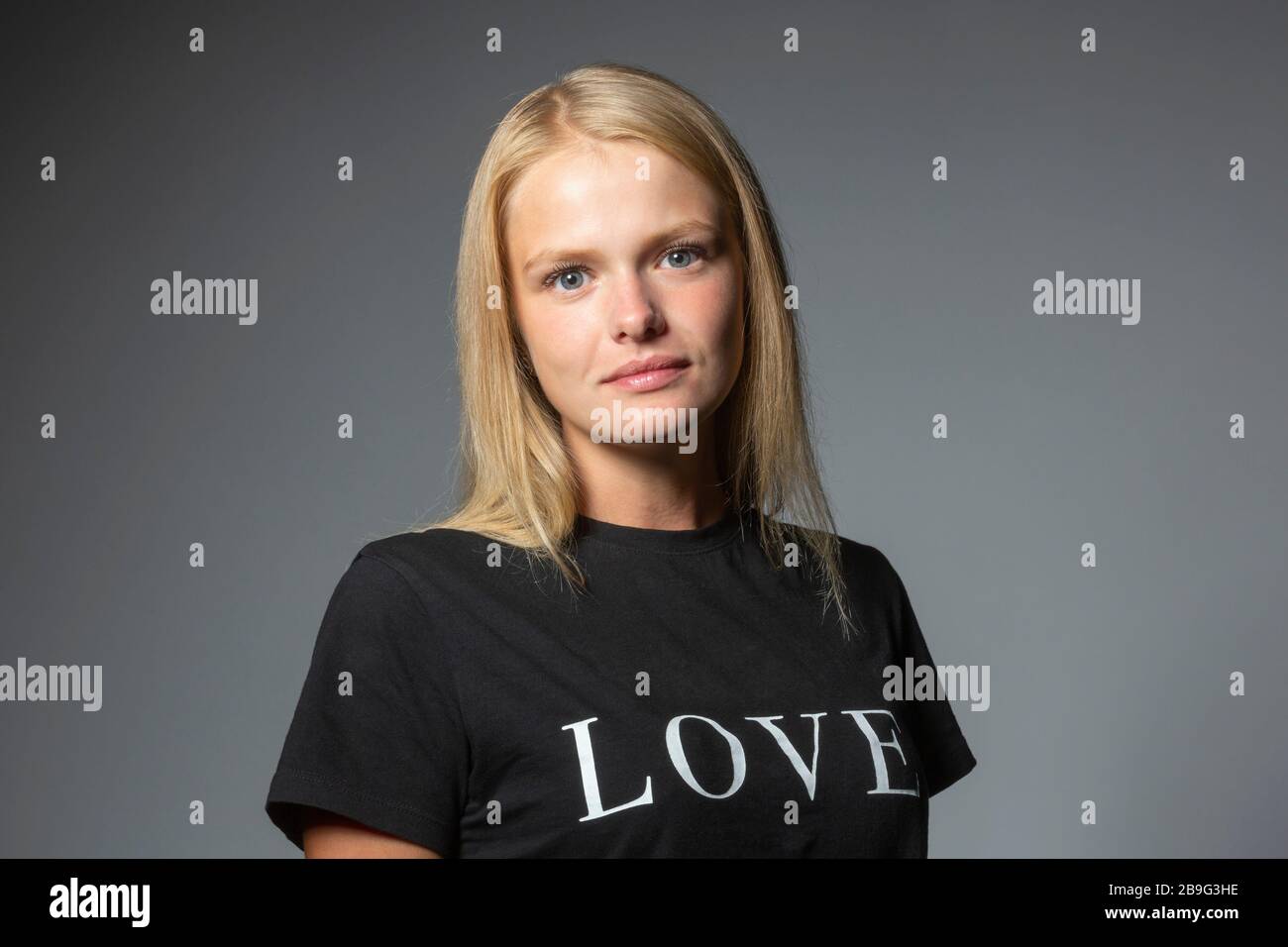 Portrait une jeune femme confiante dans un t-shirt d'amour sur fond gris Banque D'Images