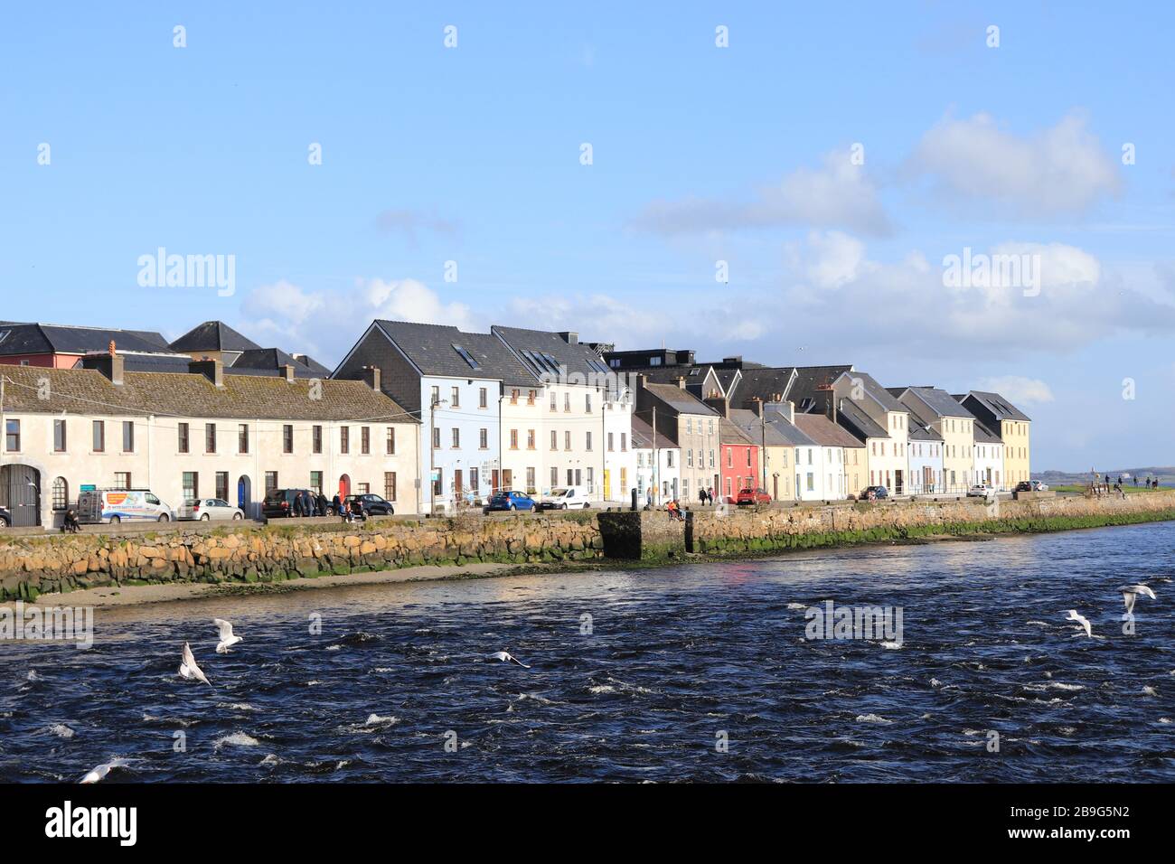 En regardant la longue promenade, la ville de Galway de l'autre côté de la rivière par une journée ensoleillée, le vol de mouettes de mer, les gens se refroidissant au loin sur le mur Banque D'Images