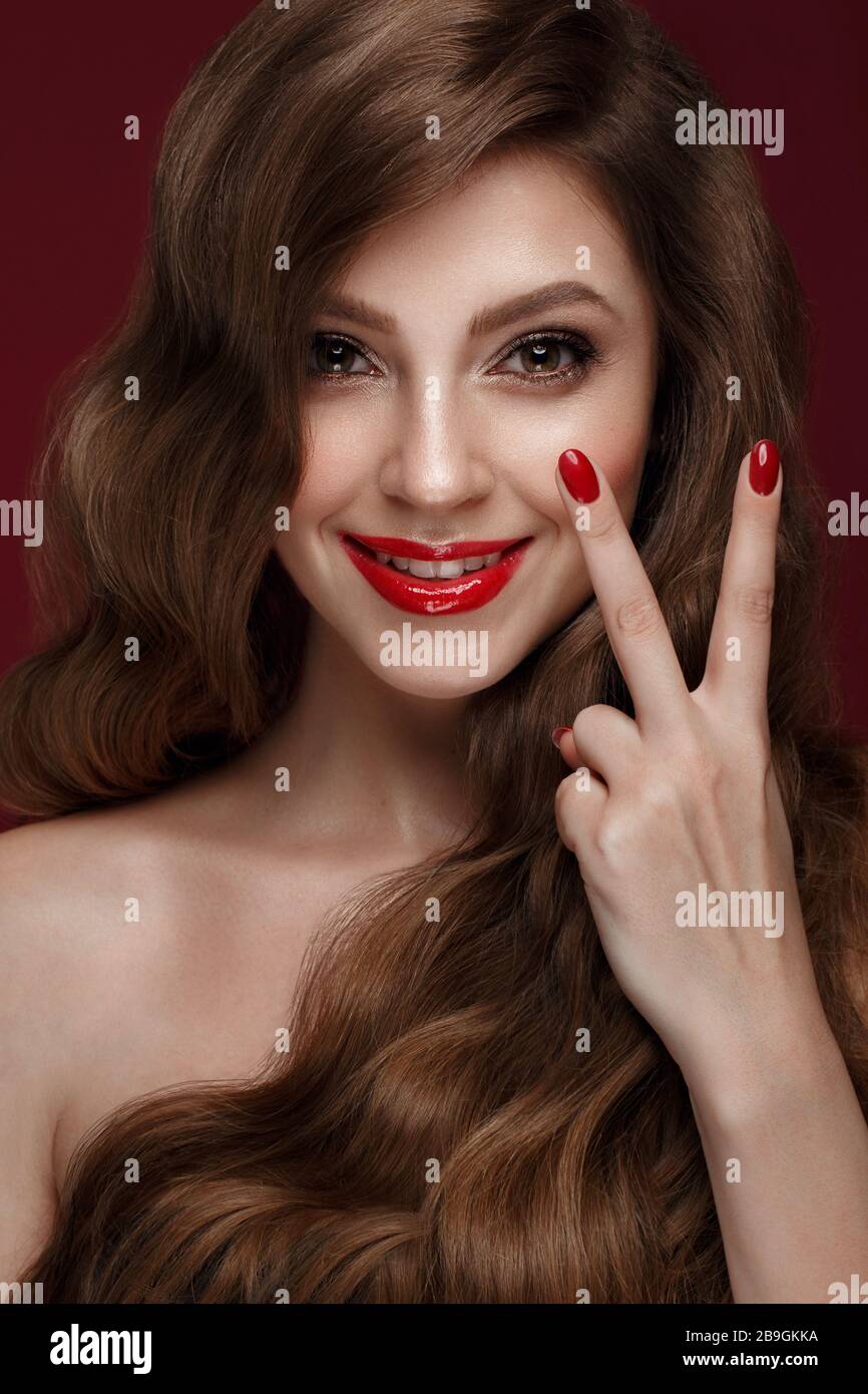 Belle fille avec un classique de la forme, des cheveux de boucles et des ongles rouges. Conception manucure. Visage de beauté. Banque D'Images