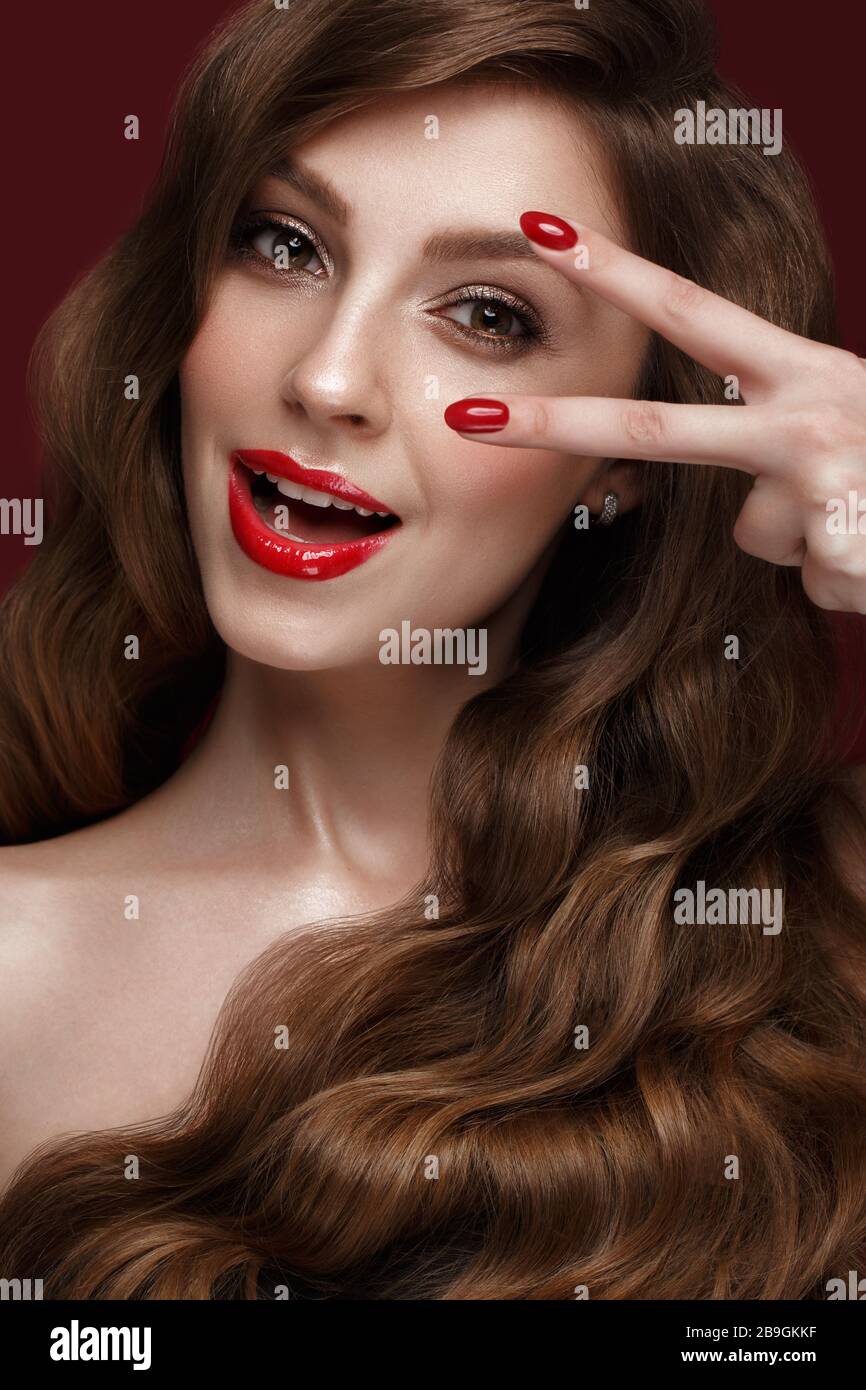 Belle fille avec un classique de la forme, des cheveux de boucles et des ongles rouges. Conception manucure. Visage de beauté. Banque D'Images