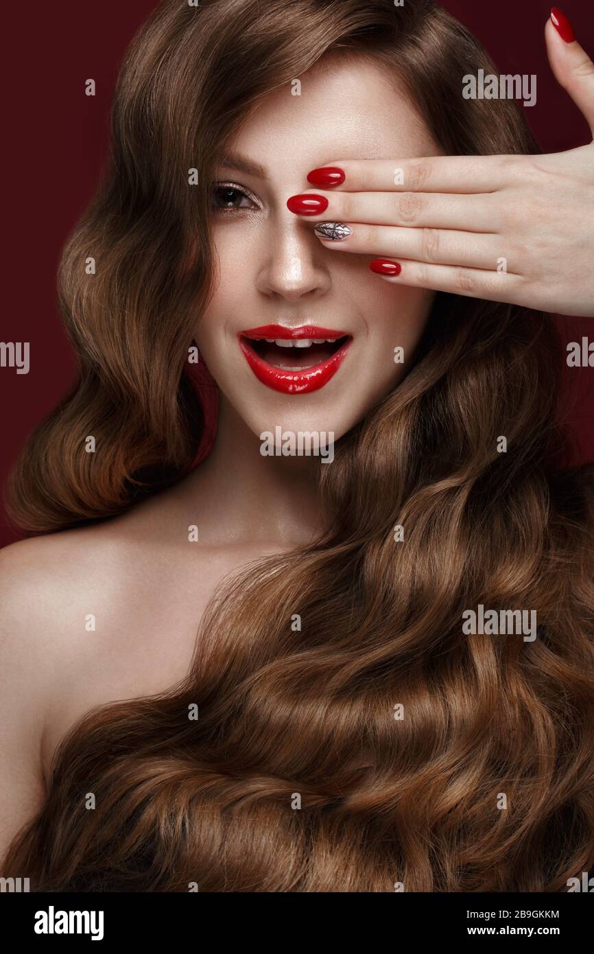 Belle fille avec un classique de la forme, des cheveux de boucles et des ongles rouges. Conception manucure. Visage de beauté. Banque D'Images