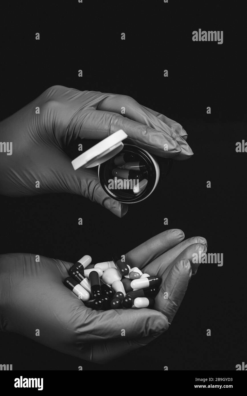 Main féminine dans des gants stériles contenant beaucoup de capsules et de pilules différentes isolées sur fond noir. Photo en noir et blanc. Banque D'Images