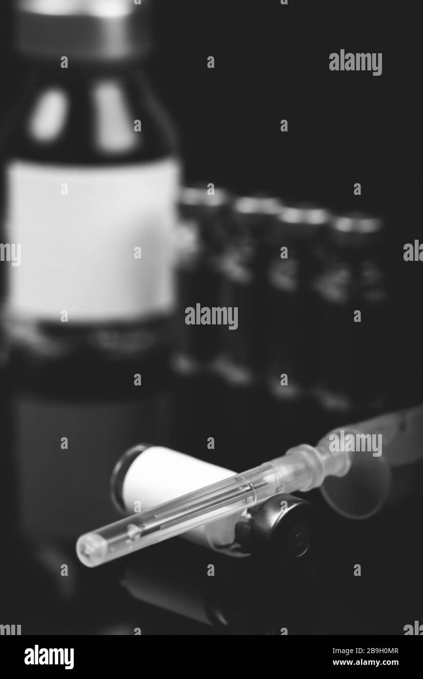 Flacons médicaux à injection avec seringue et ampoules sur fond noir. Photo en noir et blanc. Banque D'Images