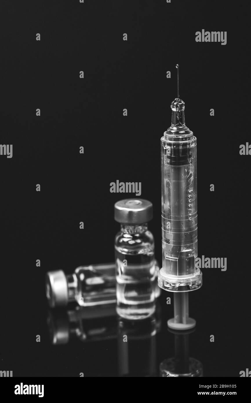 Flacons médicaux à injection avec seringue et ampoules sur fond noir. Photo en noir et blanc. Banque D'Images