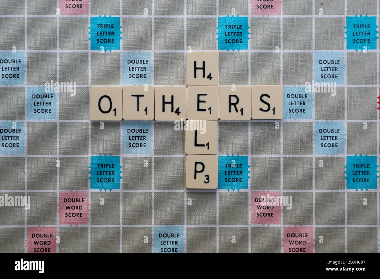 Londres, Royaume-Uni. 24 mars 2020. Scrabble Board avec des phrases et des mots liés à l'aide, la positivité et le soutien de Coronavirus. AIDEZ LES AUTRES Banque D'Images