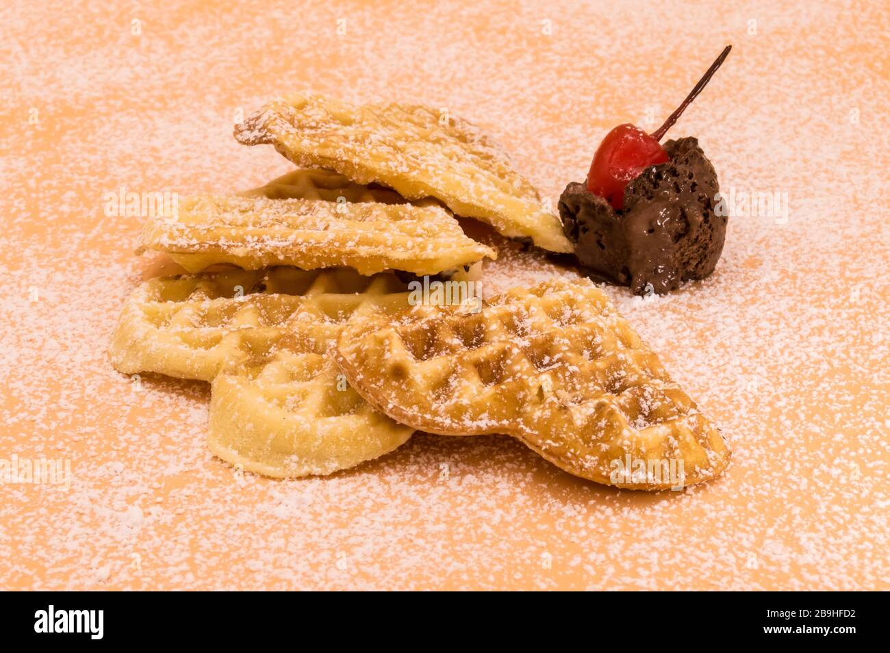 Triangle de gaufres maison avec sucre en poudre, une boule de glace au chocolat et une cerise sur fond rose, image isolée de la nourriture. Banque D'Images