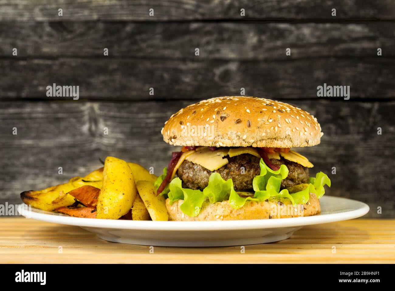 Délicieux hamburger de bœuf grillé avec des pommes de terre sur une plaque sur fond rustique en bois Banque D'Images