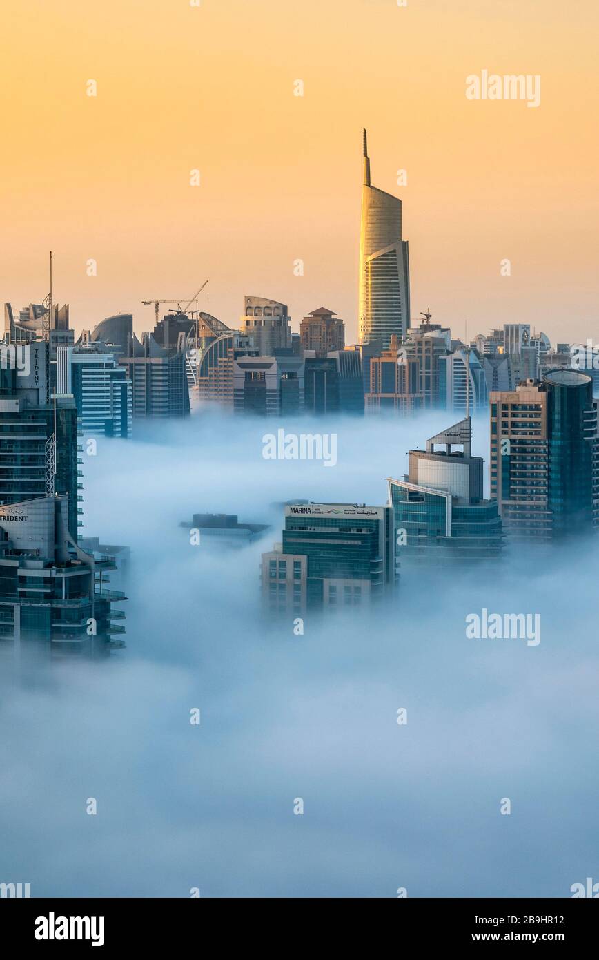 Lever de soleil brumeux avec des gratte-ciel de Dubaï Marina se dressant au dessus des nuages bas, Dubaï, Émirats Arabes Unis Banque D'Images