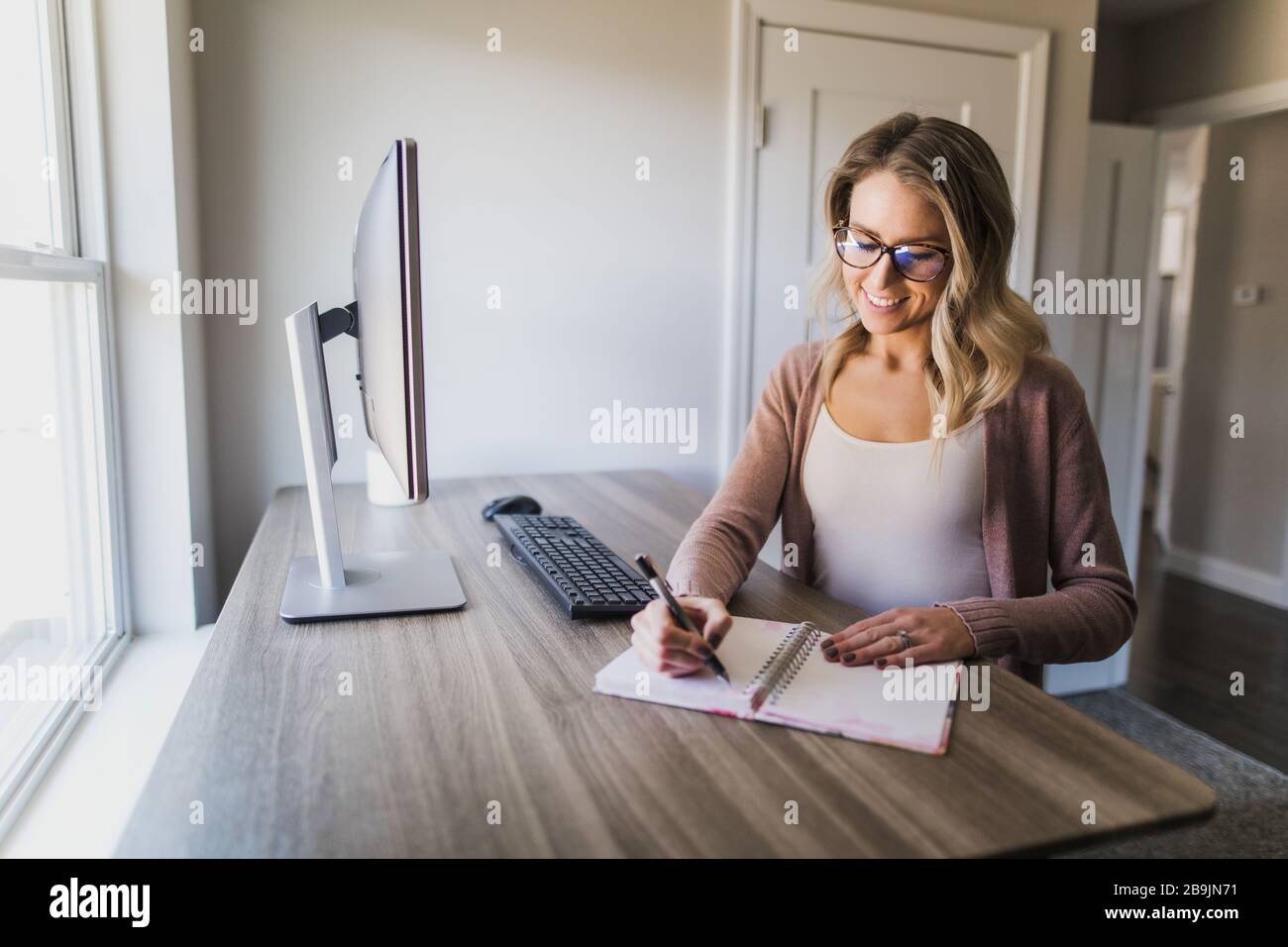Jeune femme avec des lunettes écrivant dans son carnet dans son bureau à la maison Banque D'Images