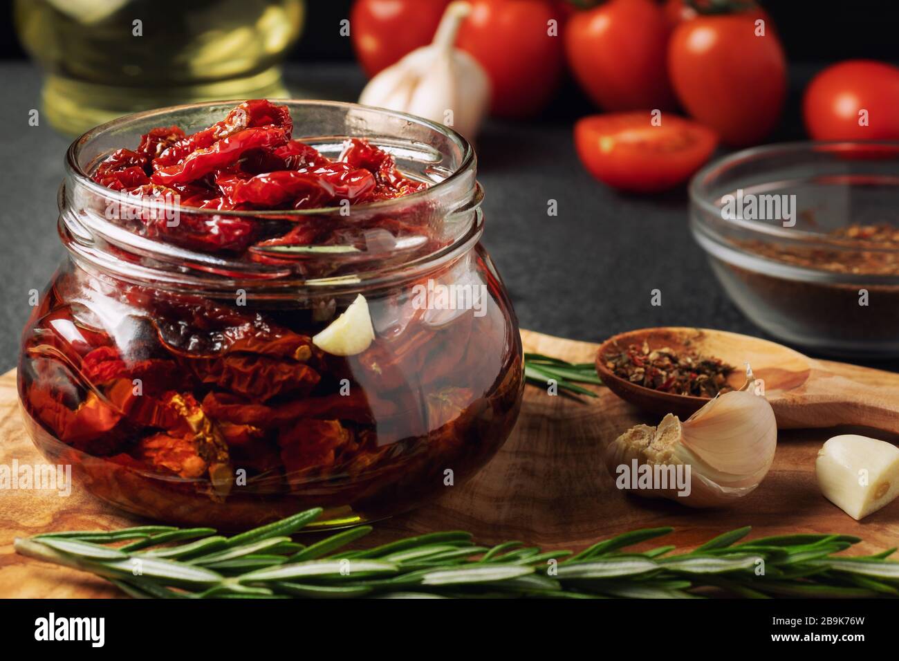 Tomates séchées au soleil avec ail, romarin et épices dans un pot en verre sur un tableau de découpe en bois d'olive. Banque D'Images