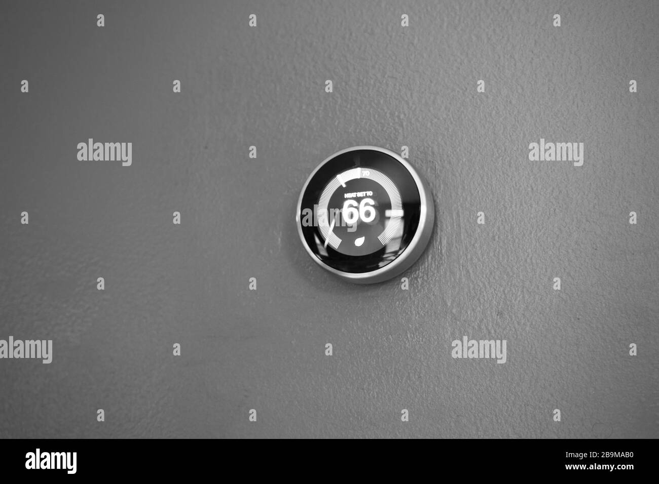 Thermostat intelligent à la maison affichant 66 degrés. Réglage de la température du thermostat sur le mur bleu pour économiser de l'argent avec la technologie verte. Noir et blanc Banque D'Images
