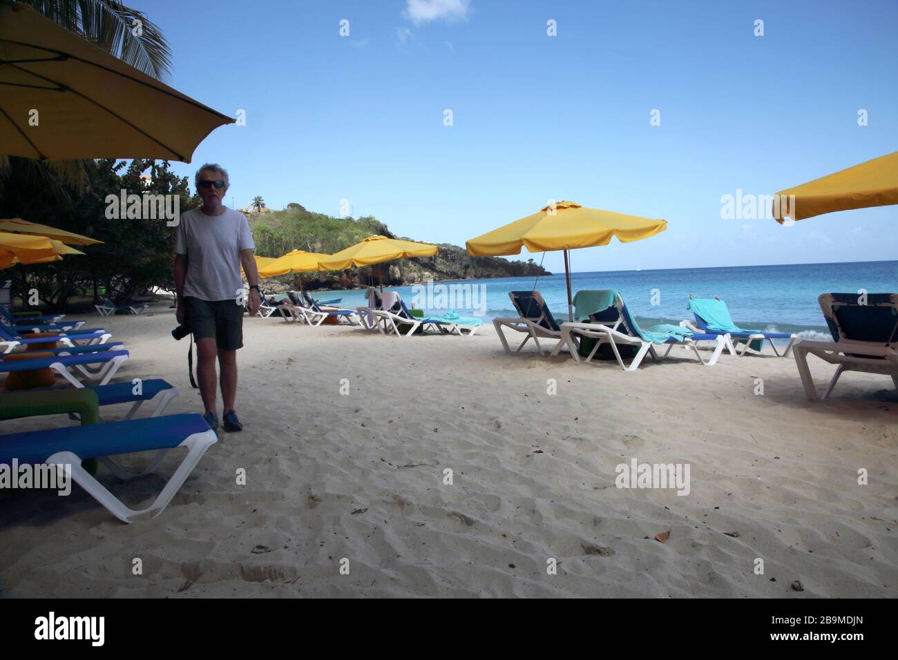 Grand Anse Beach Grenade Photographe marchant le long de la plage par des parasols et des chaises longues vides Banque D'Images
