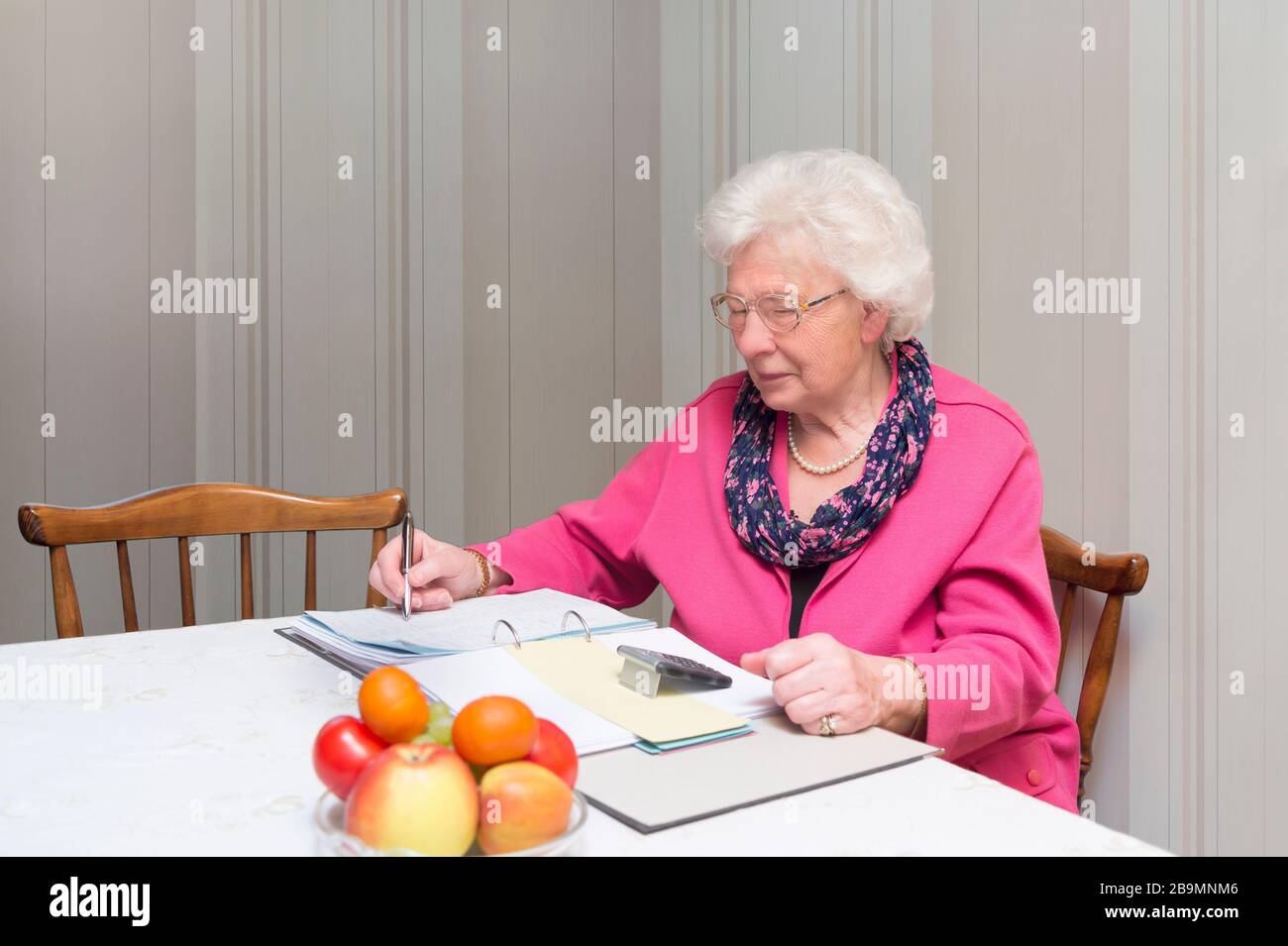 La vieille femme est assise à la table sur un dossier de fichiers et utilise la calculatrice. Chiffres et notes en arrière-plan Banque D'Images