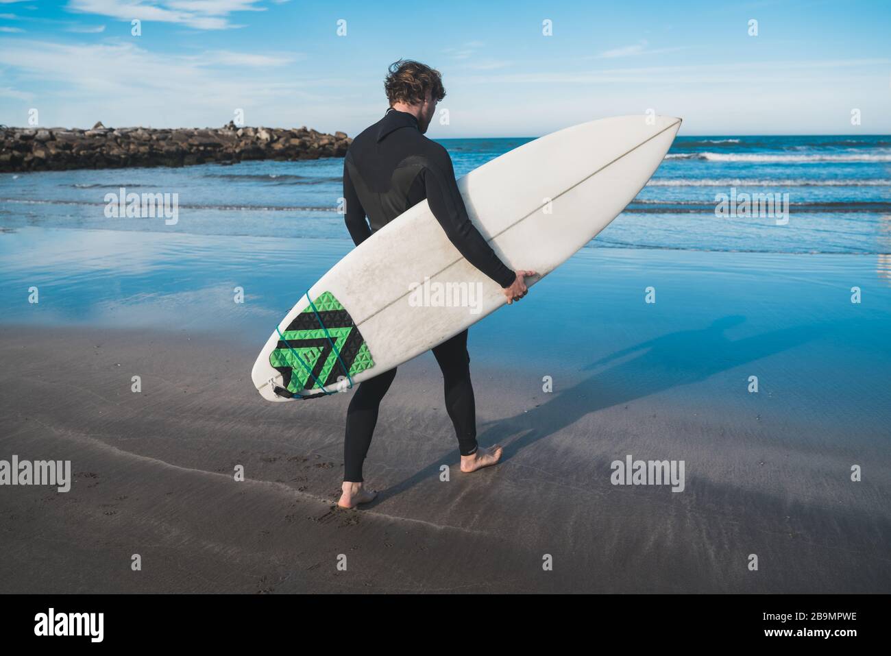 Jeune surfeur entrant dans l'eau avec son planche de surf dans un costume de surf noir. Concept de sport et de sport nautique. Banque D'Images