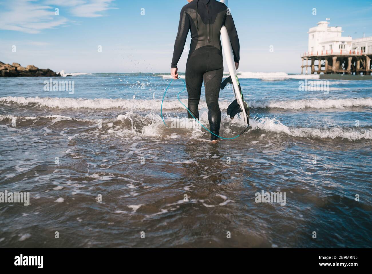 Jeune surfeur entrant dans l'eau avec son planche de surf dans un costume de surf noir. Concept de sport et de sport nautique. Banque D'Images