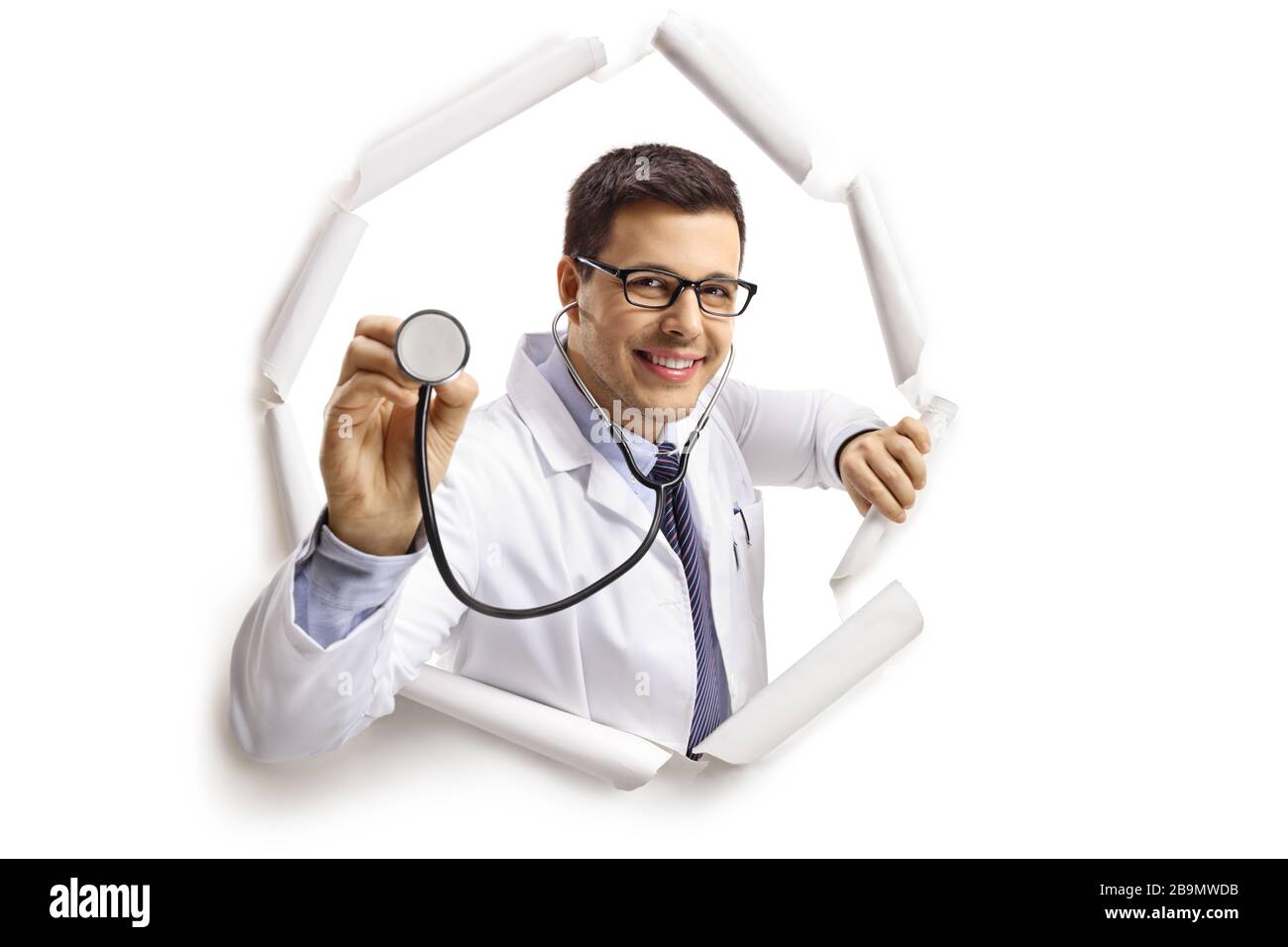 Jeune homme gai médecin avec un stéthoscope regardant par un trou de papier isolé sur fond blanc Banque D'Images