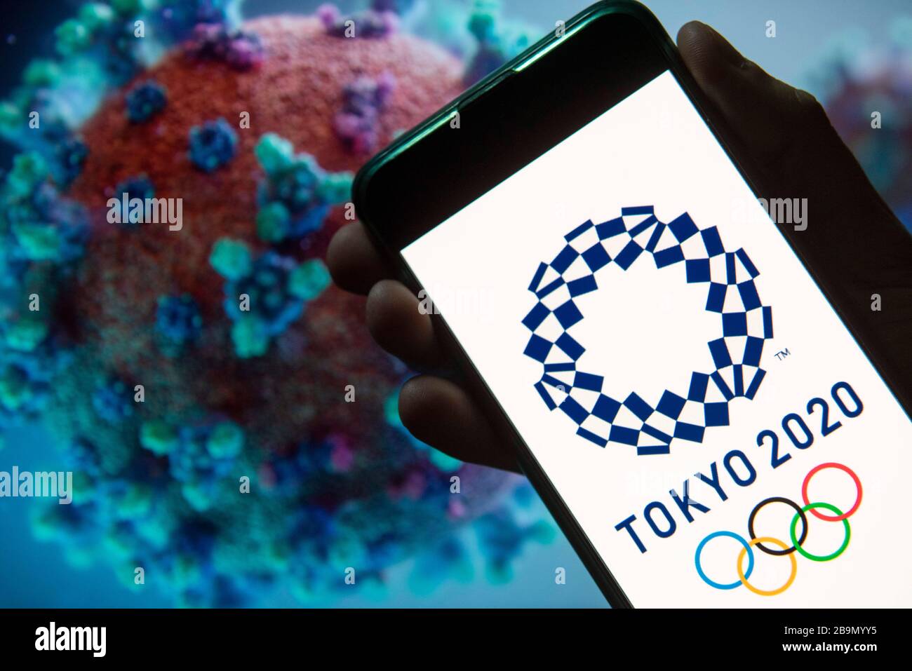 24 mars 2020, Chine: Dans cette illustration photo le logo des Jeux Olympiques de Tokyo 2020 vu sur un smartphone avec un modèle d'ordinateur du Coronavirus COVID-19 sur le fond. (Image crédit : © Budrul Chukrut/SOPA Images via ZUMA Wire) Banque D'Images