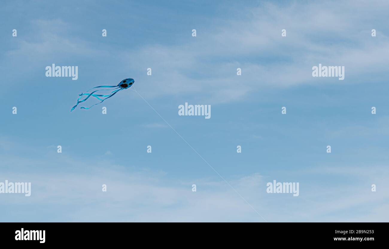 Un cerf-volant bleu volant dans le ciel blues avec des nuages Banque D'Images