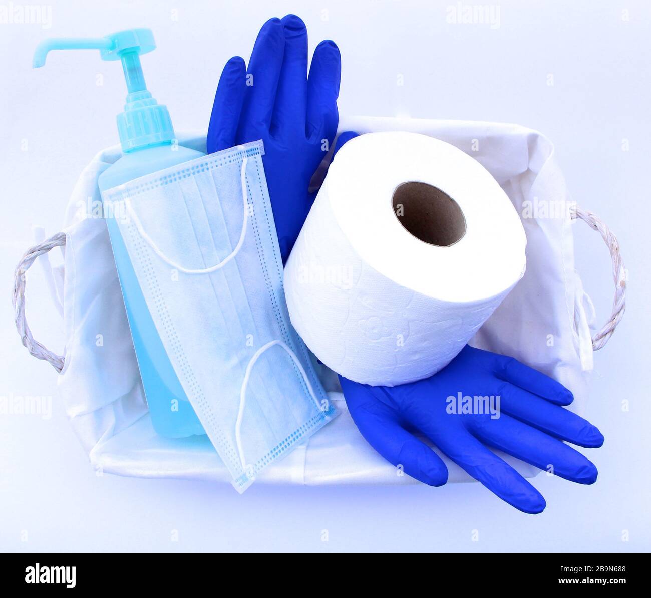 Covid-19 Novel Coronavirus Pack cadeau d'urgence dans un panier rouleau de toilettes masque médical gants en latex désinfectant pour les mains Panier blanc sur fond blanc Banque D'Images