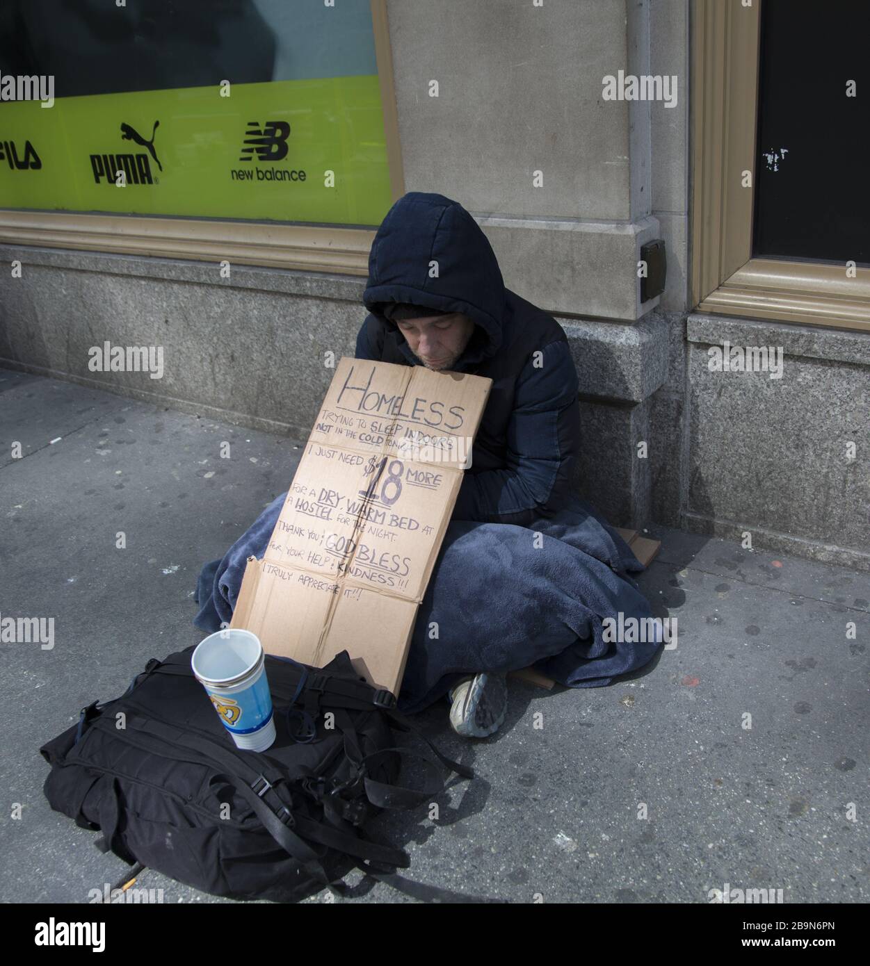 Un sans-abri qui demande de l'aide pour payer une chambre pour la nuit assise sur la 5ème Avenue dans le centre-ville de Manhattan, New York City. Banque D'Images