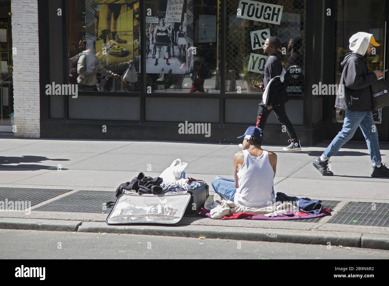 Un homme sans abri est assis sur la 6ème Avenue avec une valise ouverte qui tient ses affaires. New York. Banque D'Images