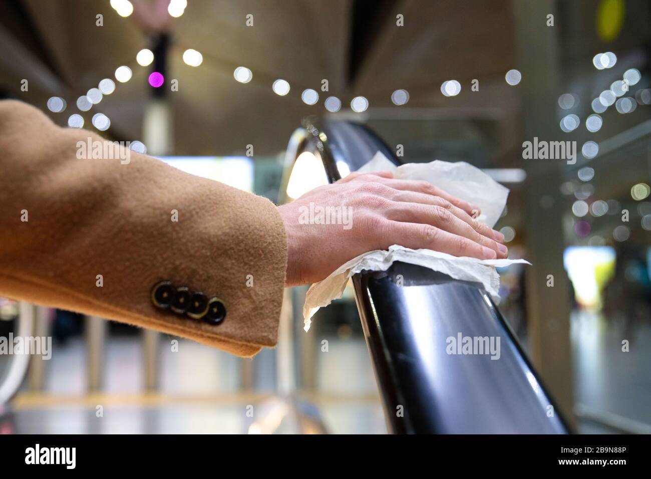 Près de la main de l'homme tient une main courante de l'escalator dans le terminal de l'aéroport à travers une serviette, pour vous protéger du contact avec les virus, les germes pendant un co Banque D'Images