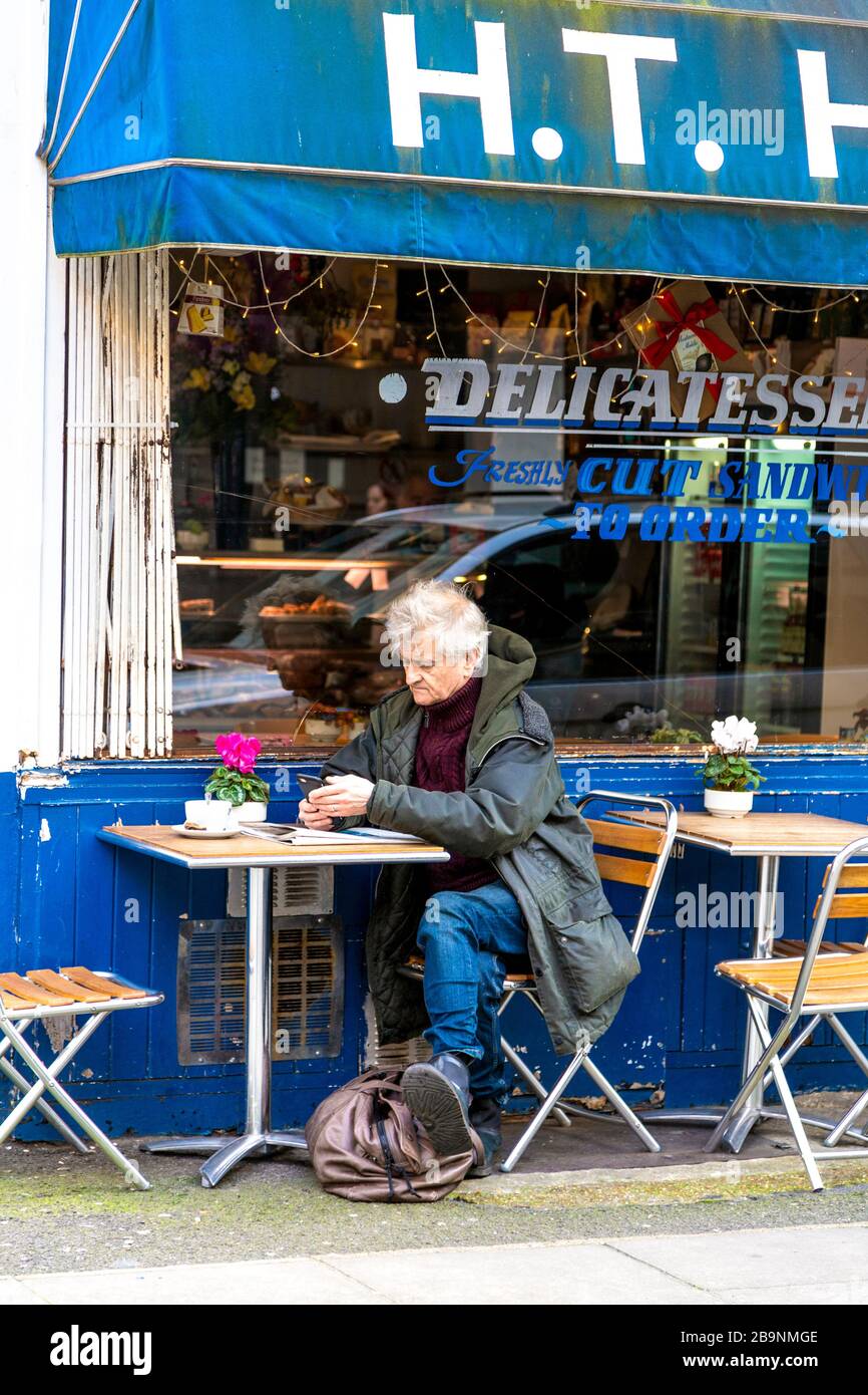 Homme assis à l'extérieur de la boutique de sandwichs H T Harris et épicerie fine, Fitzrovia, Londres, Royaume-Uni Banque D'Images