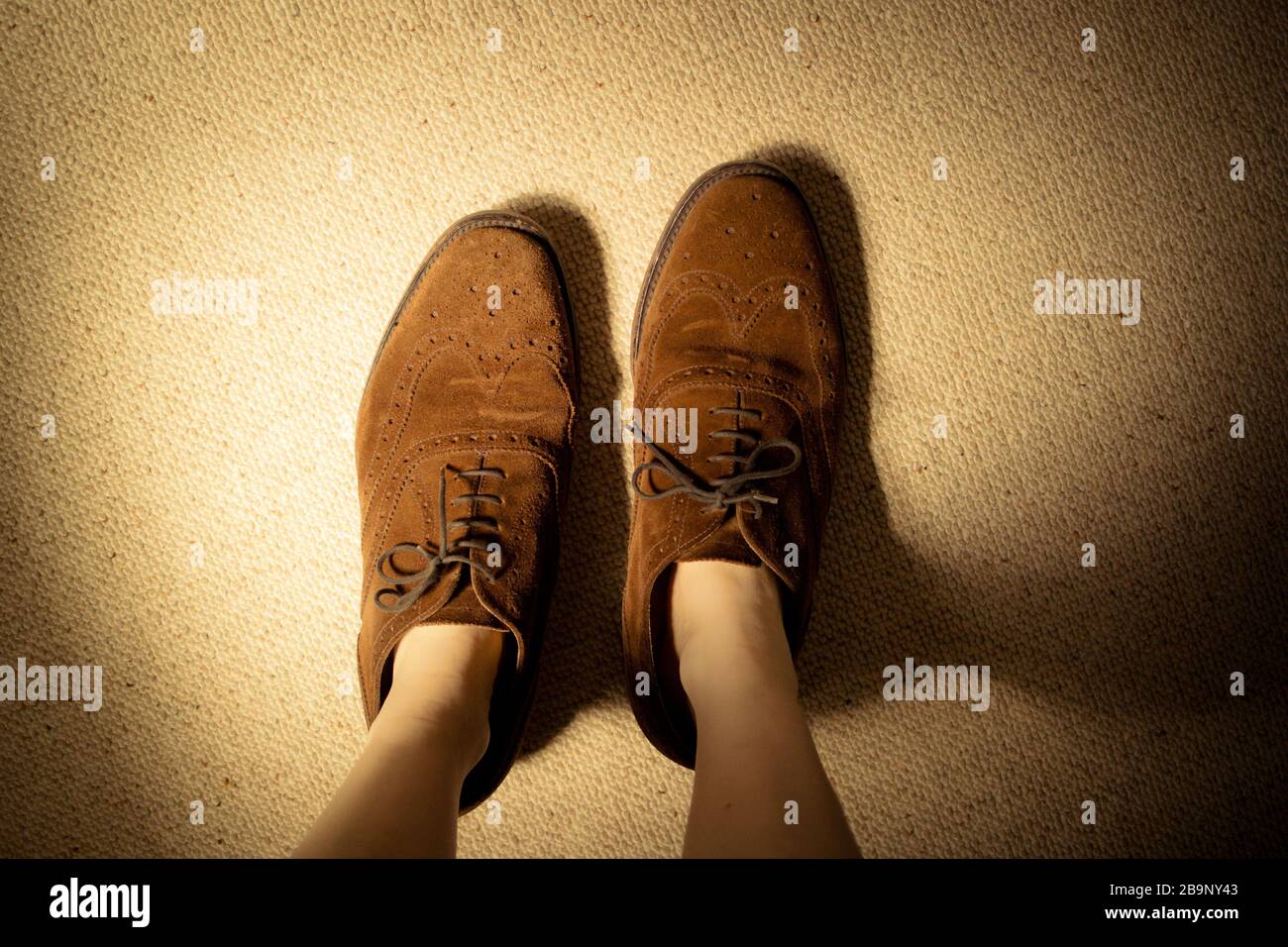 Regarder vers le bas les pieds d'une femme ou d'un enfant portant de grands hommes en daim brun chaussures de rigue qui sont beaucoup trop grands. Banque D'Images