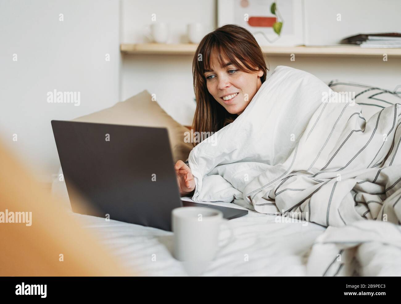 Travail jeune femme brunette freelance dans des vêtements décontractés avec  ordinateur portable et tasse de thé réveil dans le lit à la maison dans un  séjour intérieur lumineux à la maison Photo