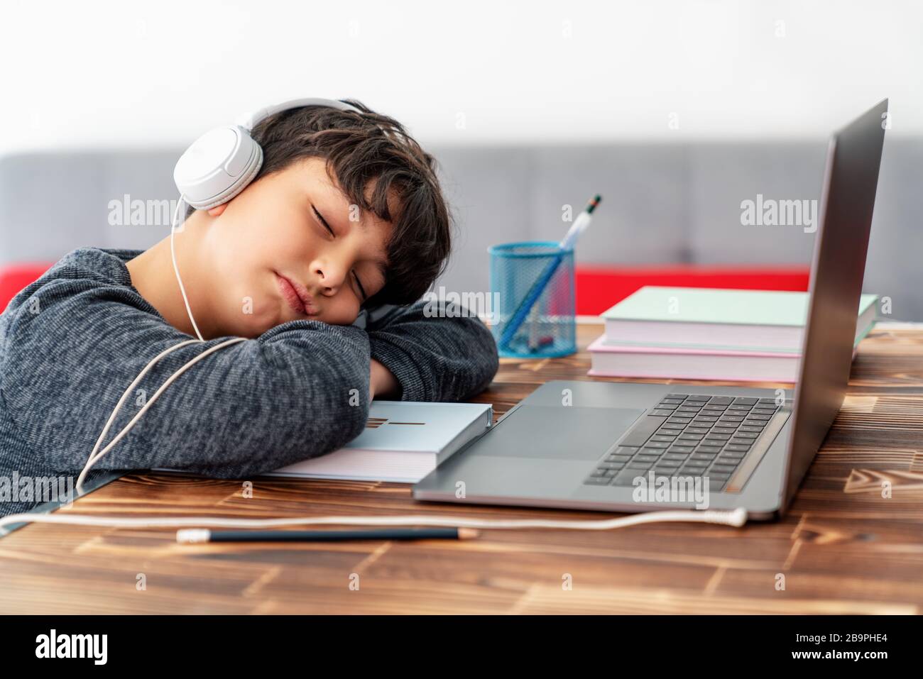Un petit garçon fatigué a somnolent devant l'ordinateur portable pendant qu'il étudie à la maison en ligne Banque D'Images