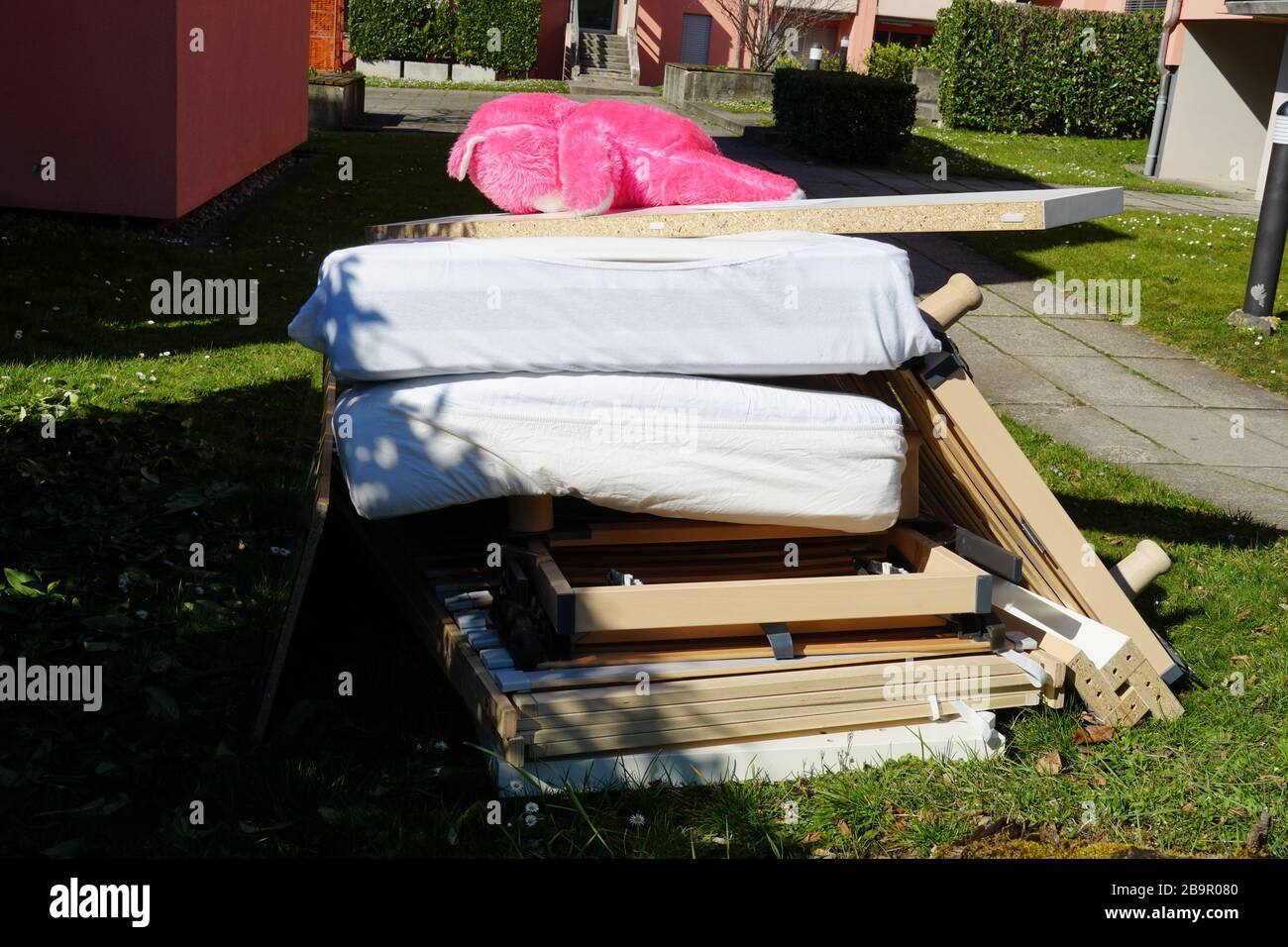 Vieux meubles disjoints sur une pile avec un grand ours en peluche rose couché sur elle. Le tas se compose principalement de la construction de lit et de matelas. Banque D'Images