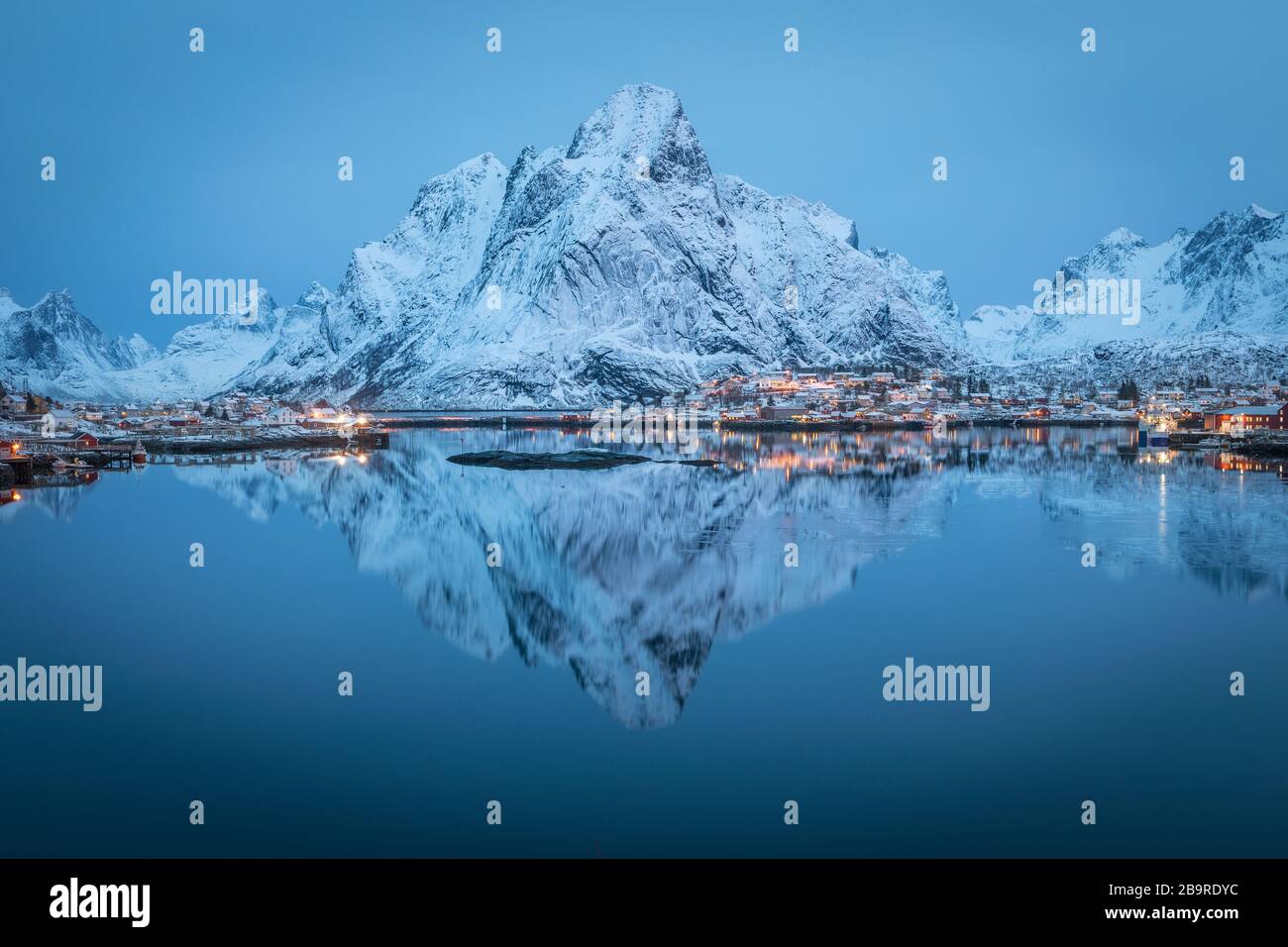 Grande montagne enneigée reflétée dans les eaux calmes et froides du fjord d'Extrême-Nord. Village de pêcheurs à l'aube. Scène de sérénité des Lofoten, cirlce arctique. Banque D'Images
