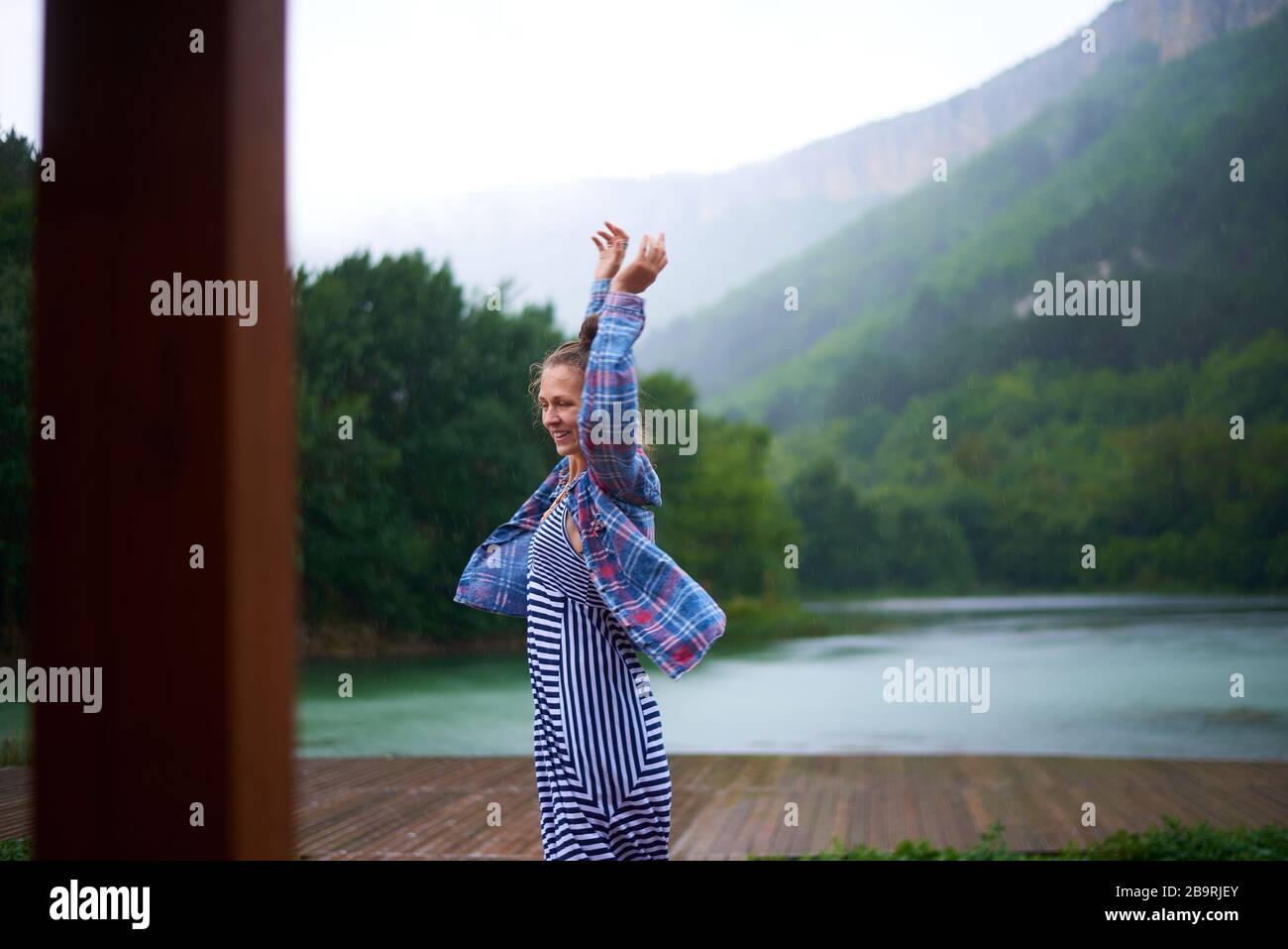 Femme de randonnée décontractée sous la pluie dansant près du lac dans les montagnes. Expression franche et authentique. Banque D'Images