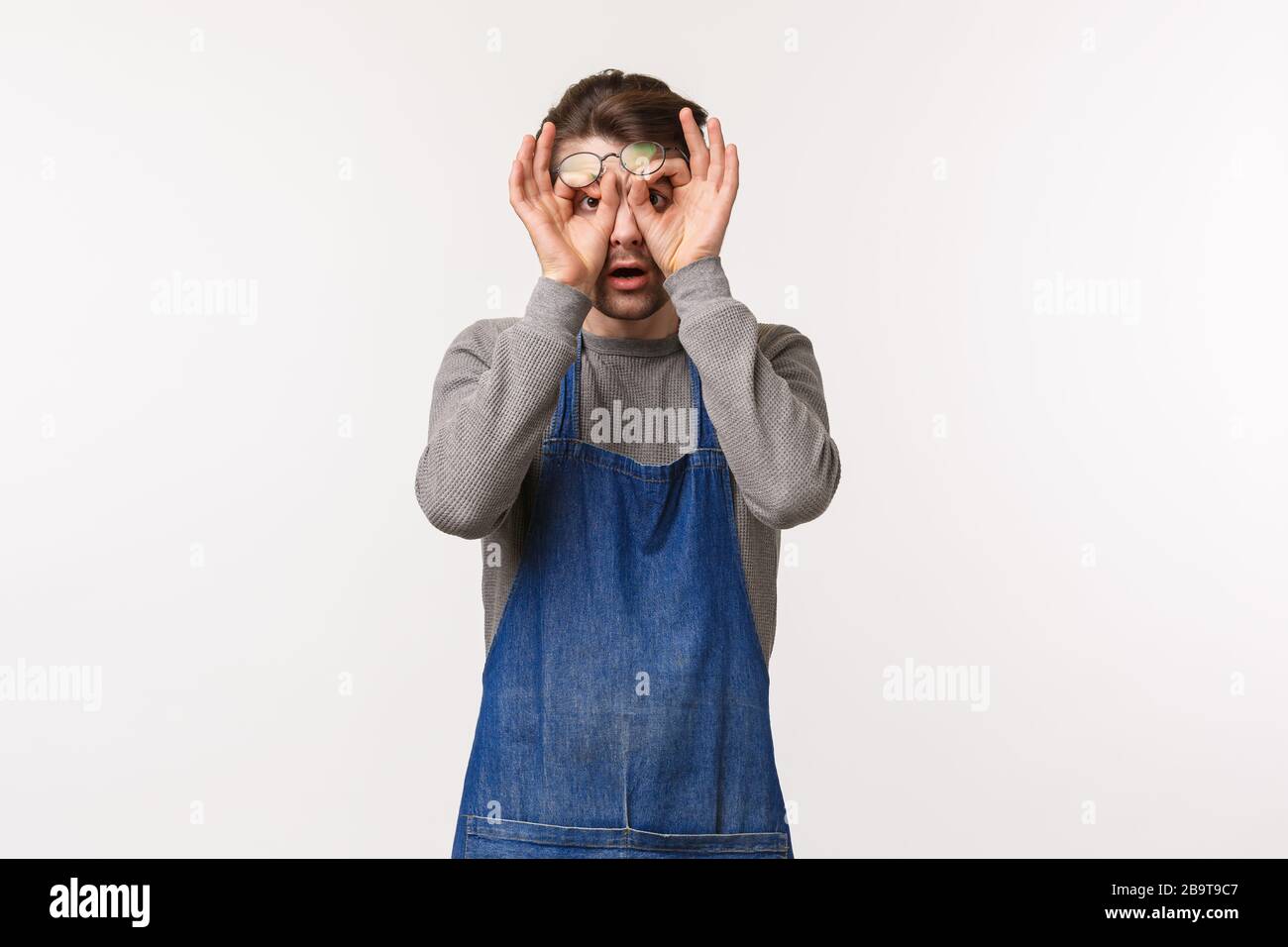 Portrait de jeune homme choqué et étonné dans le tablier, l'employé du café frotte les yeux de l'incrédulité, affamant impressionné et surpris à quelque chose Banque D'Images