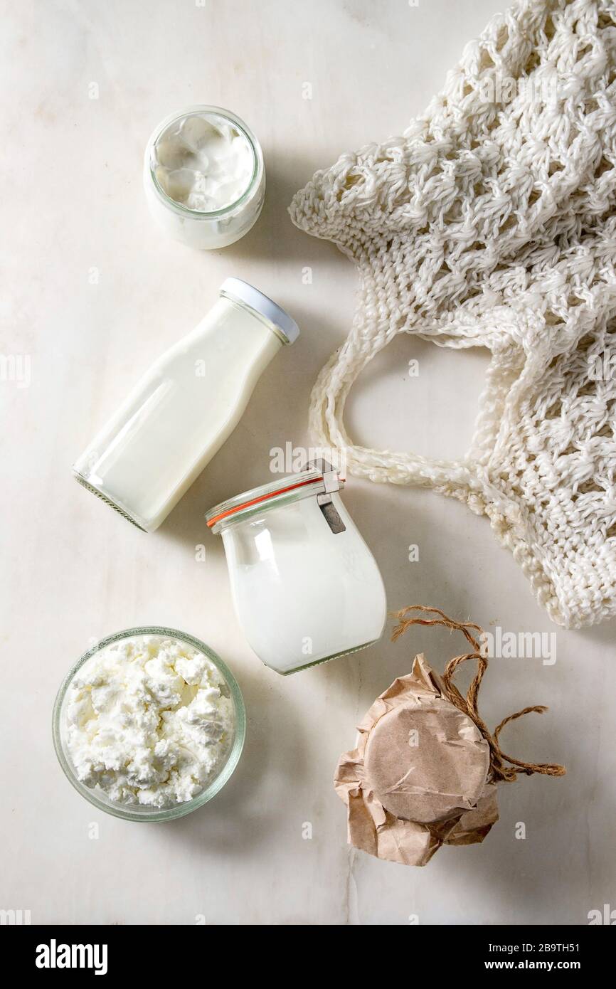 Ensemble de produits laitiers de la ferme, fromage cottage, crème de lait, yaourt dans des pots en verre réutilisables et bouteille avec sac tricoté sur fond de marbre blanc. Réfrigérateur ECO Banque D'Images