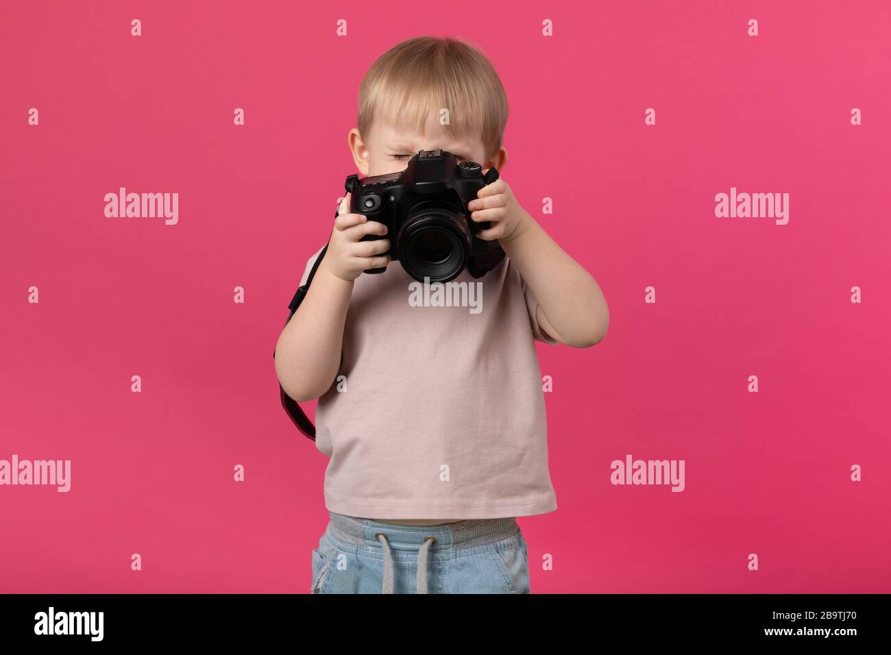 Un enfant garçon d'apparence européenne des photos blondes avec un appareil photo. Gros plan studio tourné sur un fond rose pour des articles sur le recrutement pour les écoles Banque D'Images