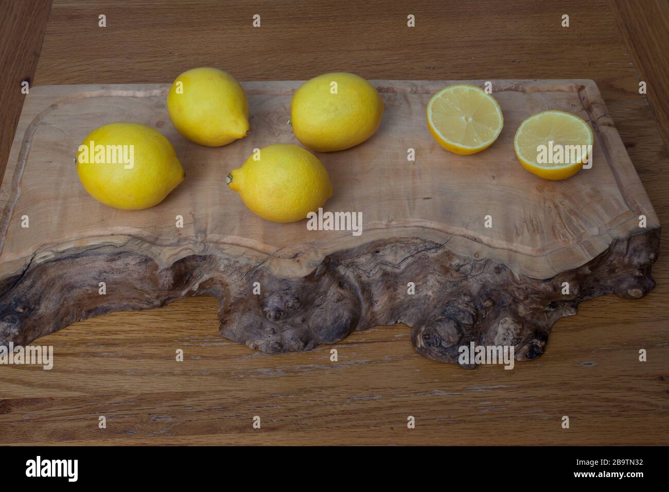 Citrons sur une planche à découper en bois, entiers et en deux moitiés Banque D'Images