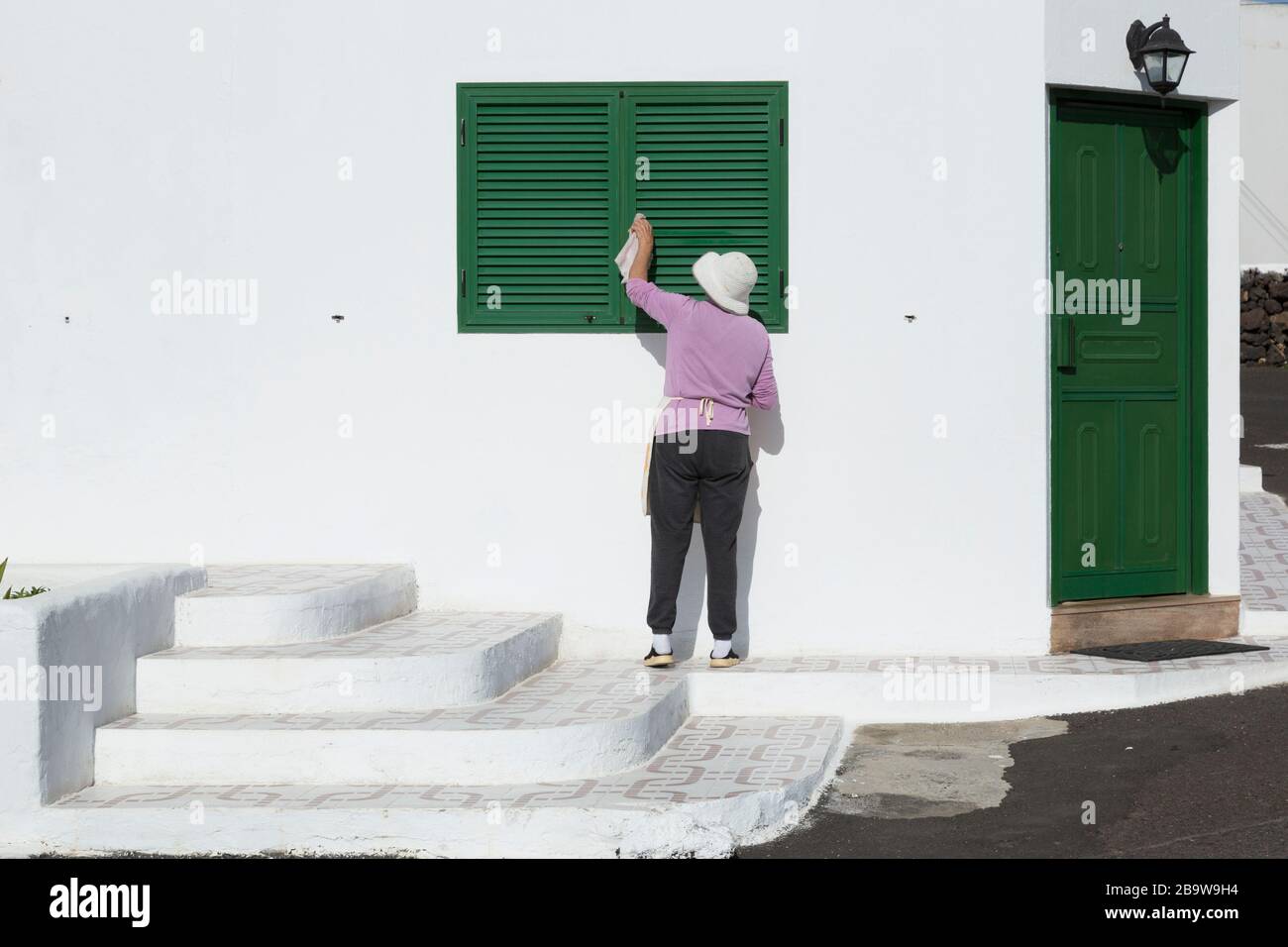 Une femme qui nettoie les volets d'une maison blanchie à la chaux à Uga, Lanzarote, îles Canaries, Espagne Banque D'Images