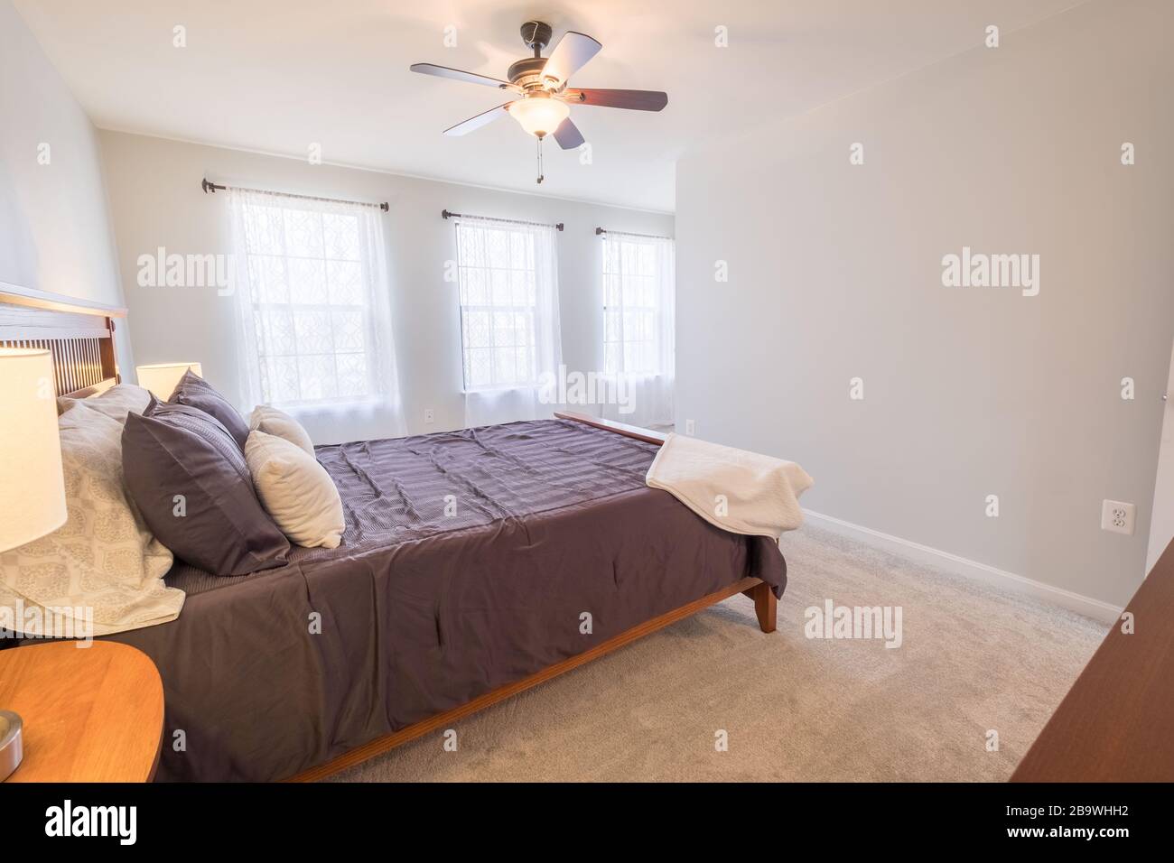Belle photo d'une chambre avec un lit double, une lampe sur la table et un ventilateur de plafond avec lumière Banque D'Images