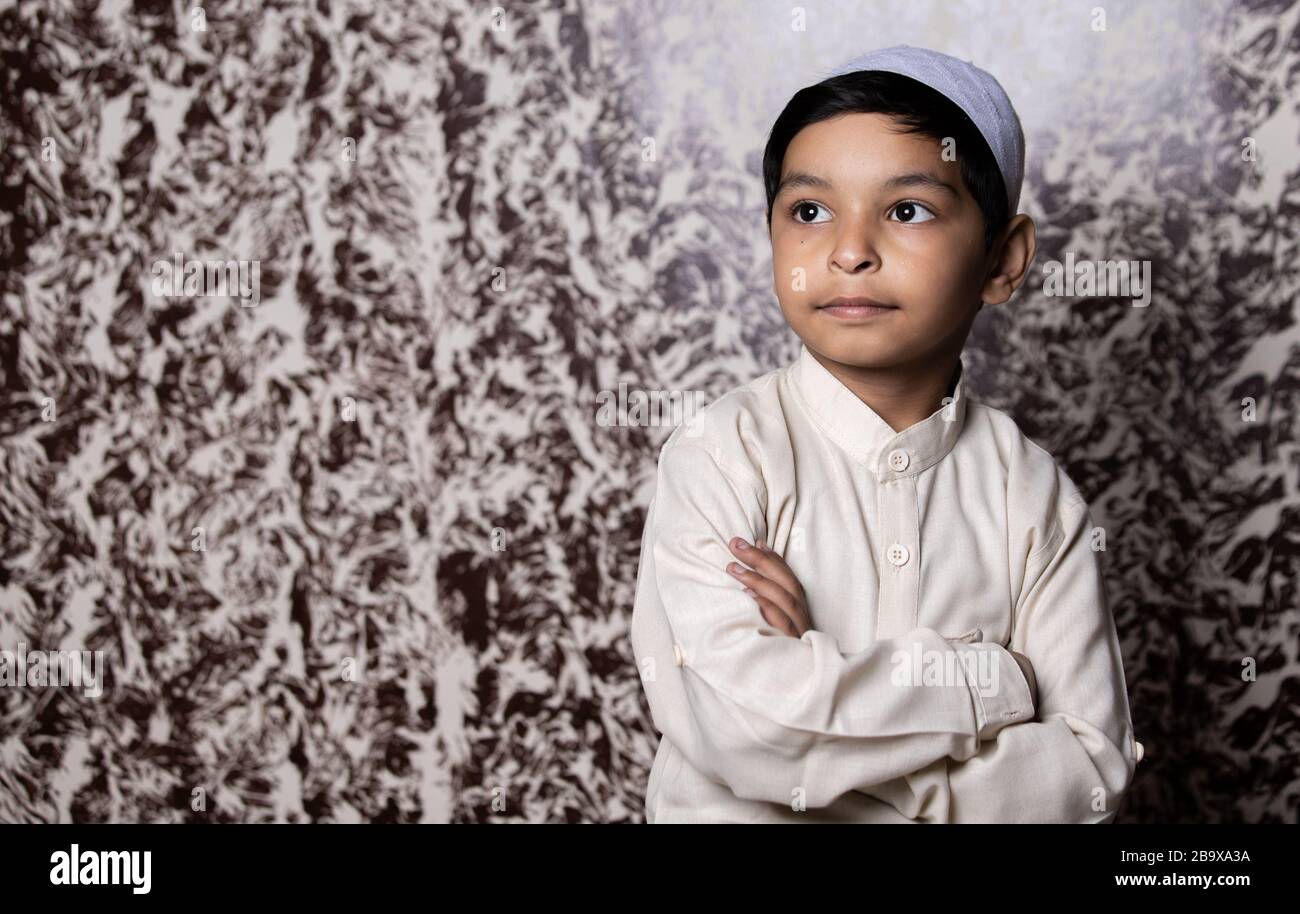 Portrait d'enfant musulman avec casquette musulmane et robe ethnique blanche donnant l'expression vers la lumière Banque D'Images