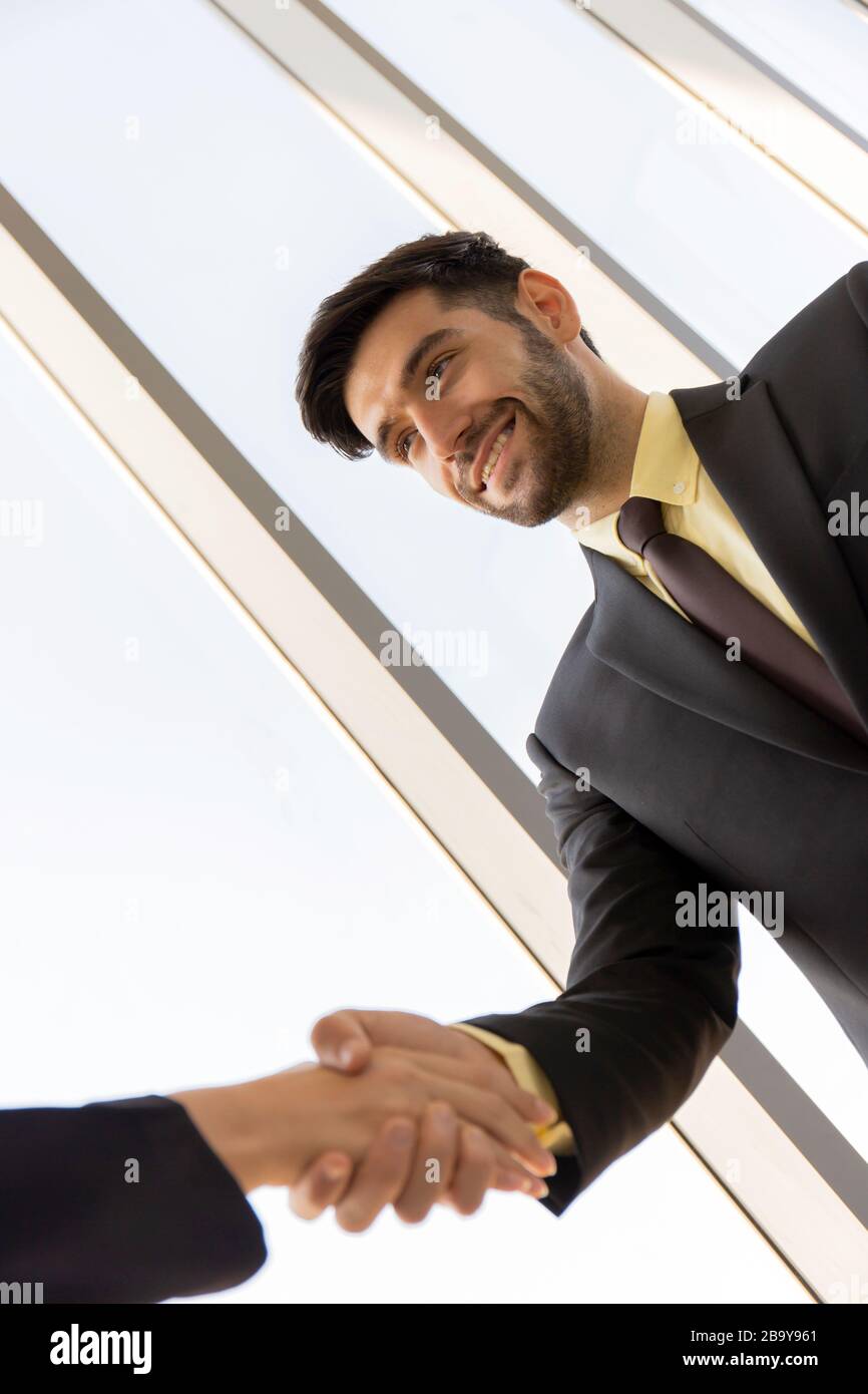 Deux jeunes gens d'affaires sont habilement vêtus d'un costume et d'une cravate, tenant les mains, montrant des entreprises séparées avec des visages souriants heureux. Banque D'Images