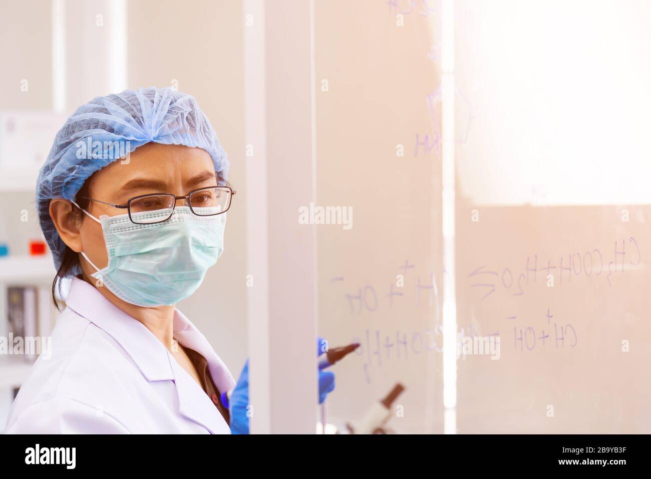 Une scientifique asiatique féminine rédige la formule de calcul de la chimie sur le verre clair dans un laboratoire. Banque D'Images