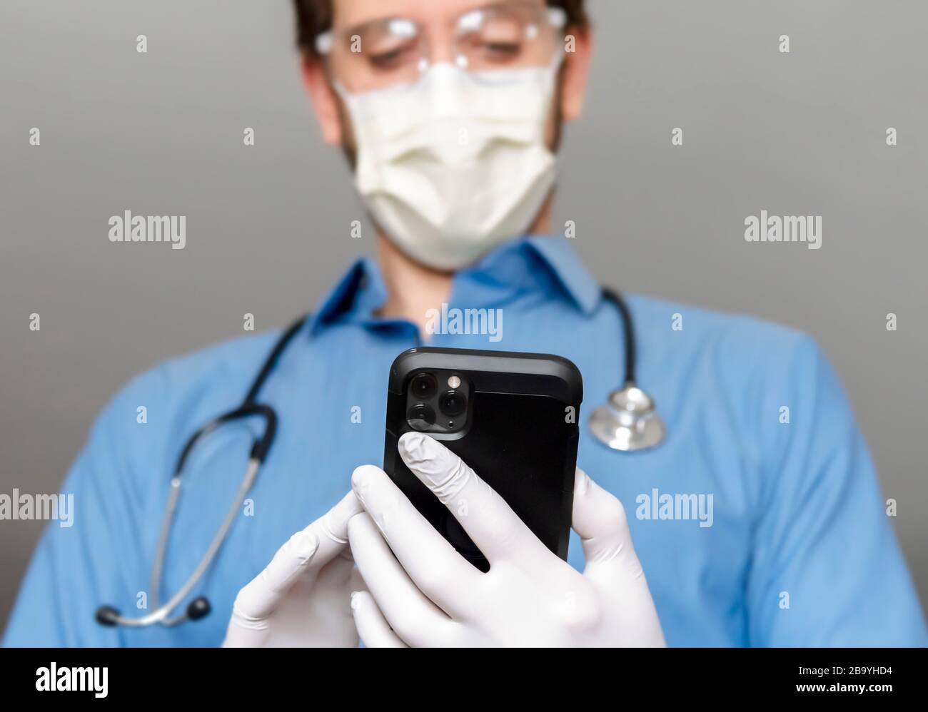 Le prestataire de soins de santé porte un équipement de protection tout en vérifiant les symptômes sur un smartphone. Banque D'Images