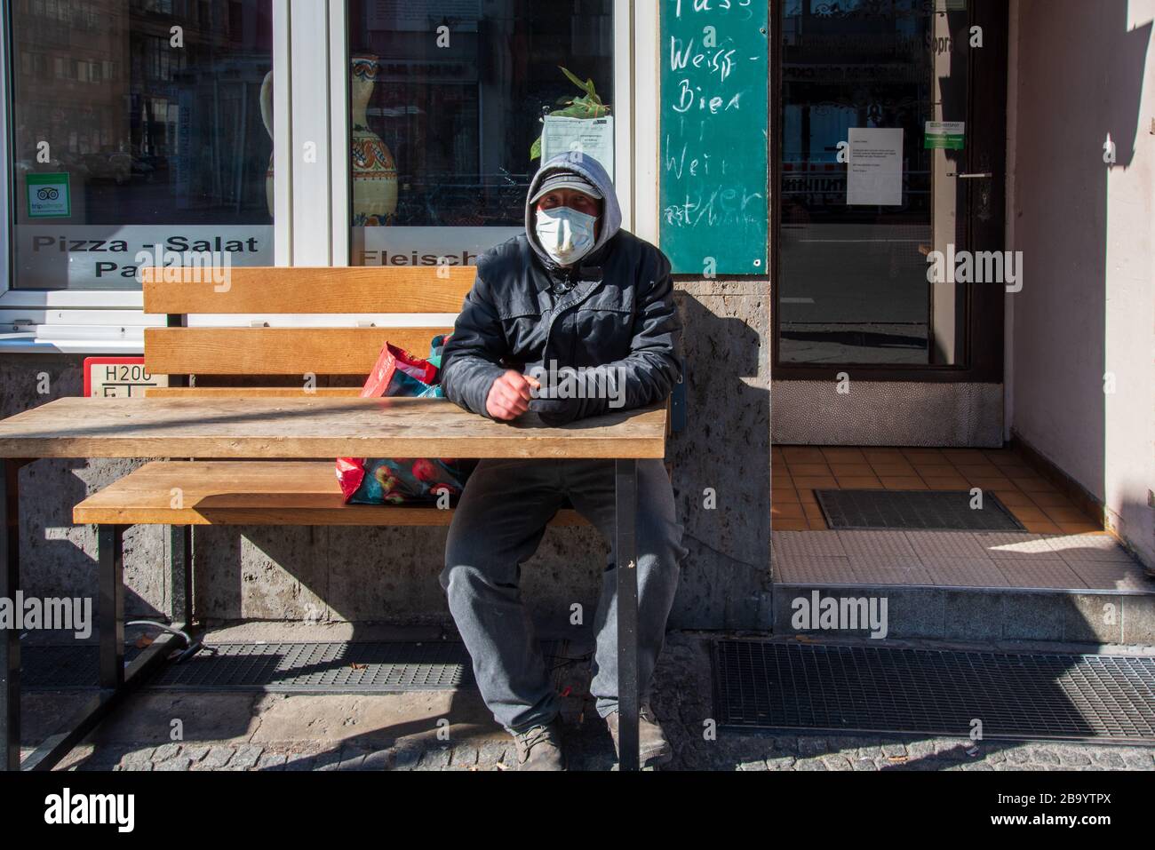 Homme portant un visage tout en se reposant sur un banc à l'extérieur d'un restaurant fermé dans le centre de Berlin pendant la crise corona Banque D'Images