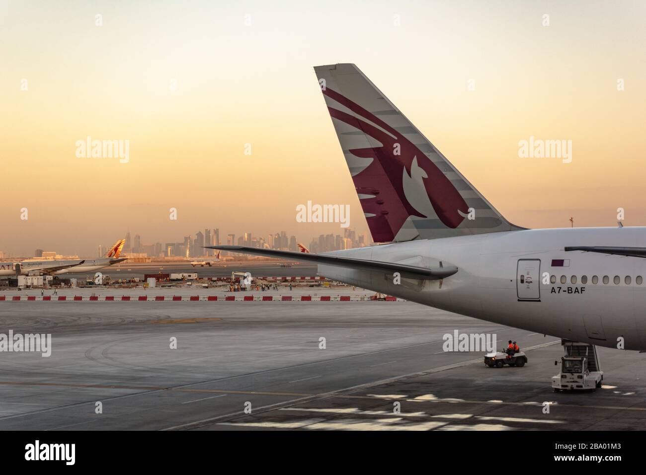 La queue d'un avion Boeing 777 de Qatar Airways à l'aéroport de Doha tôt le matin avec la ville Banque D'Images