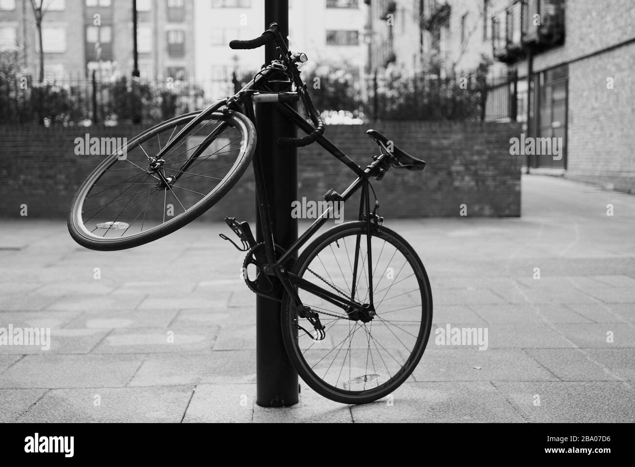 Photo en noir et blanc d'un vélo enchaîné à un poteau de lampe à Londres. Le vélo de course est incliné pour s'adapter au verrou de sécurité. Banque D'Images